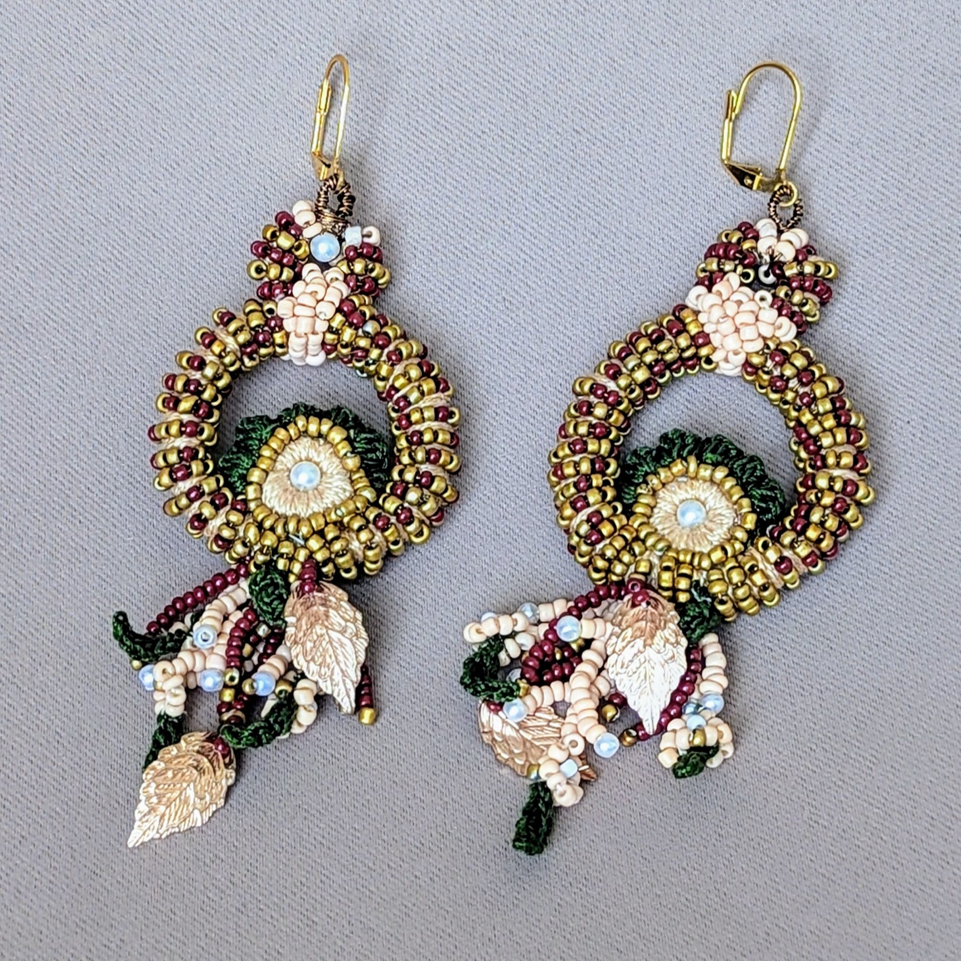 A one of a kind artisan handcrafted pair of Indian bridal earrings from sustainable UK brand Mayaani Jewellery. These stunning earrings feature traditional Indian colours of red, green and gold, woven together to create a peacock worthy shape. Crafted with intricate hand bead embroidery, hand crochet and meticulous wire wrapping, they showcase the finest quality materials. 