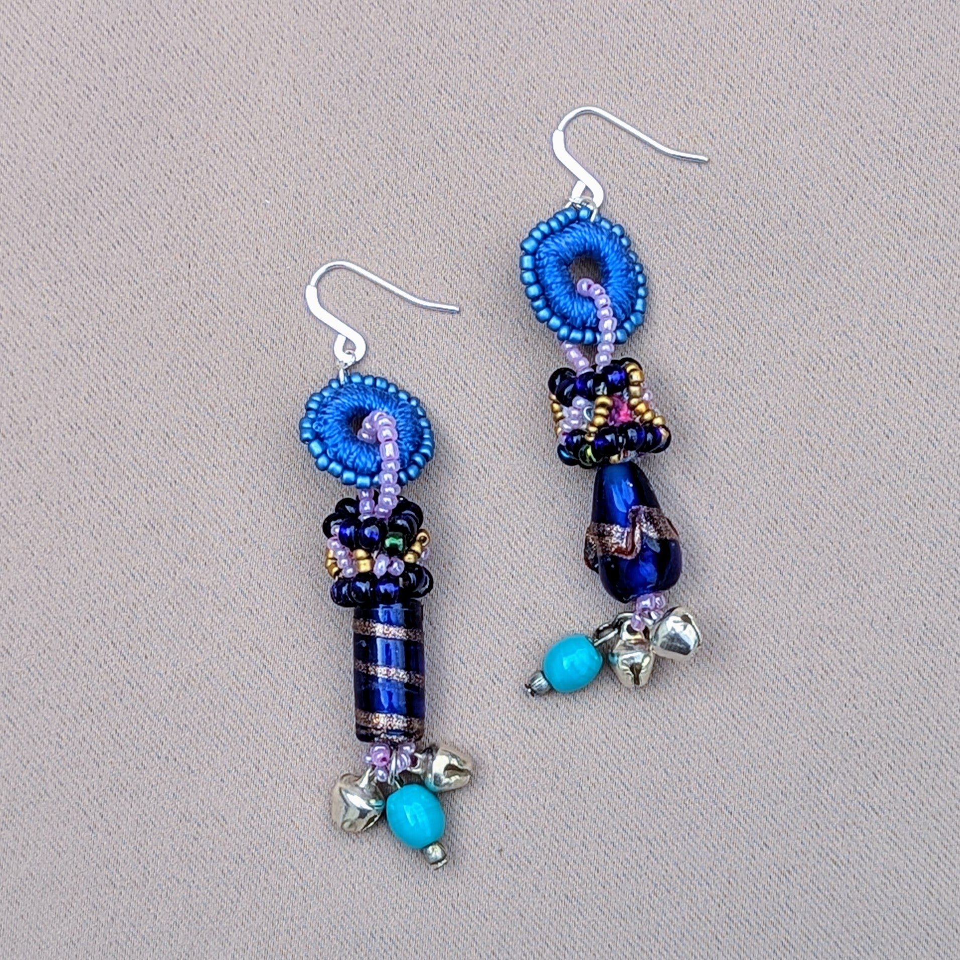 Unique artisan handcrafted earrings by Mayaani Jewellery UK, inspired by Indian culture and crafted using scrap beads created from in-house designer Megha's jewellery-making-process. These striking earrings feature blue and purple hand beadwork, along with vibrant turquoise accents. The design is completed with solid silver ghungroo bells, symbolising classical Indian dance heritage, blending tradition with contemporary sustainable fashion.