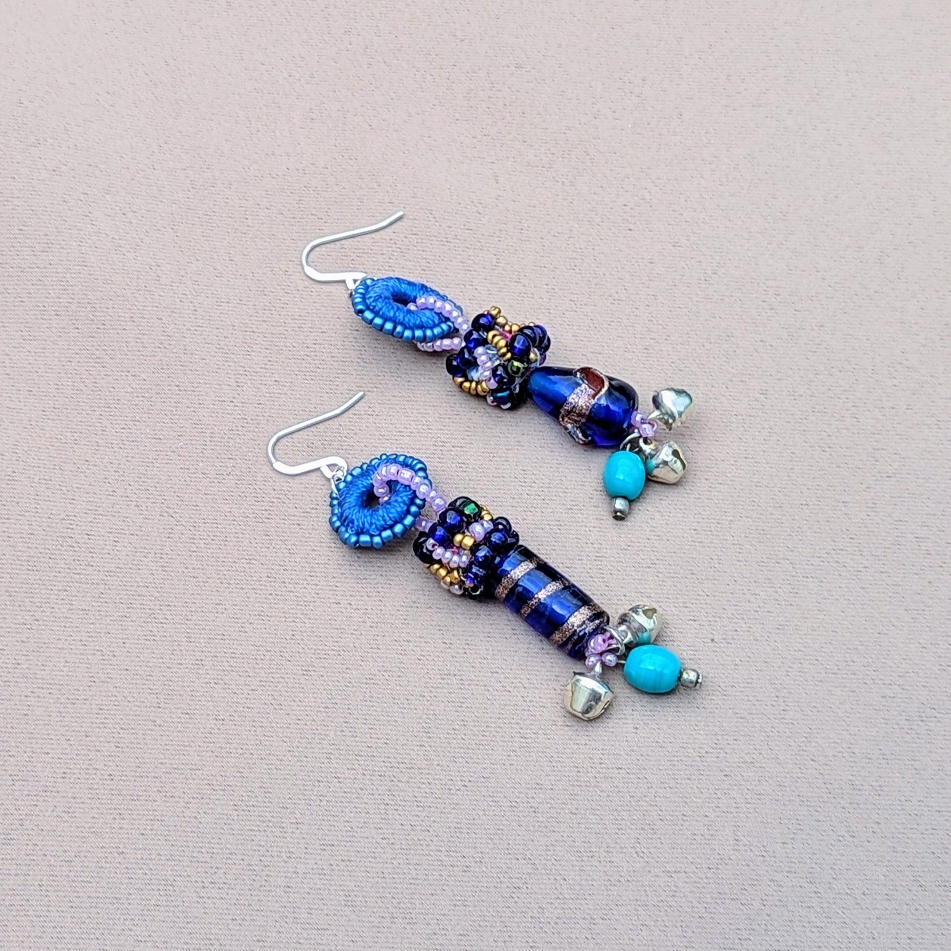 Scrap beads hand made from the waste produced by Mayaani Jewellery UK, adorn this pair of unique earrings reflecting a fusion of tradition and sustainability. The blue and purple beadwork is paired with hand crochet and turquoise accents complemented by solid silver ghungroo bells which pay homage to classical Indian dance culture.