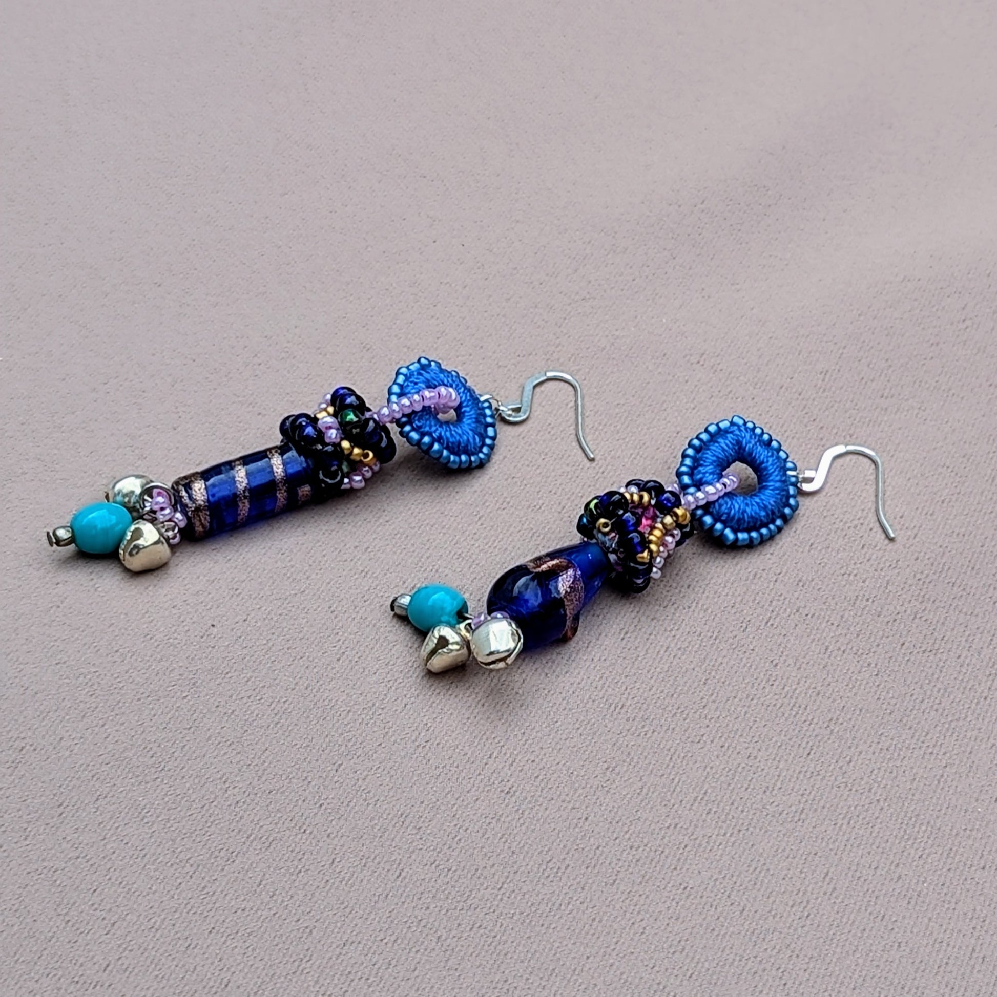 These unique earrings by Mayaani Jewellery UK feature beads hand crafted from recycled materials alongside hand crochet, intricate purple and blue beadwork, turquoise accents and solid silver ghungroo bells. Embrace a beautiful nod to classical Indian dance in this beautiful fusion of sustainability and cultural artistry.