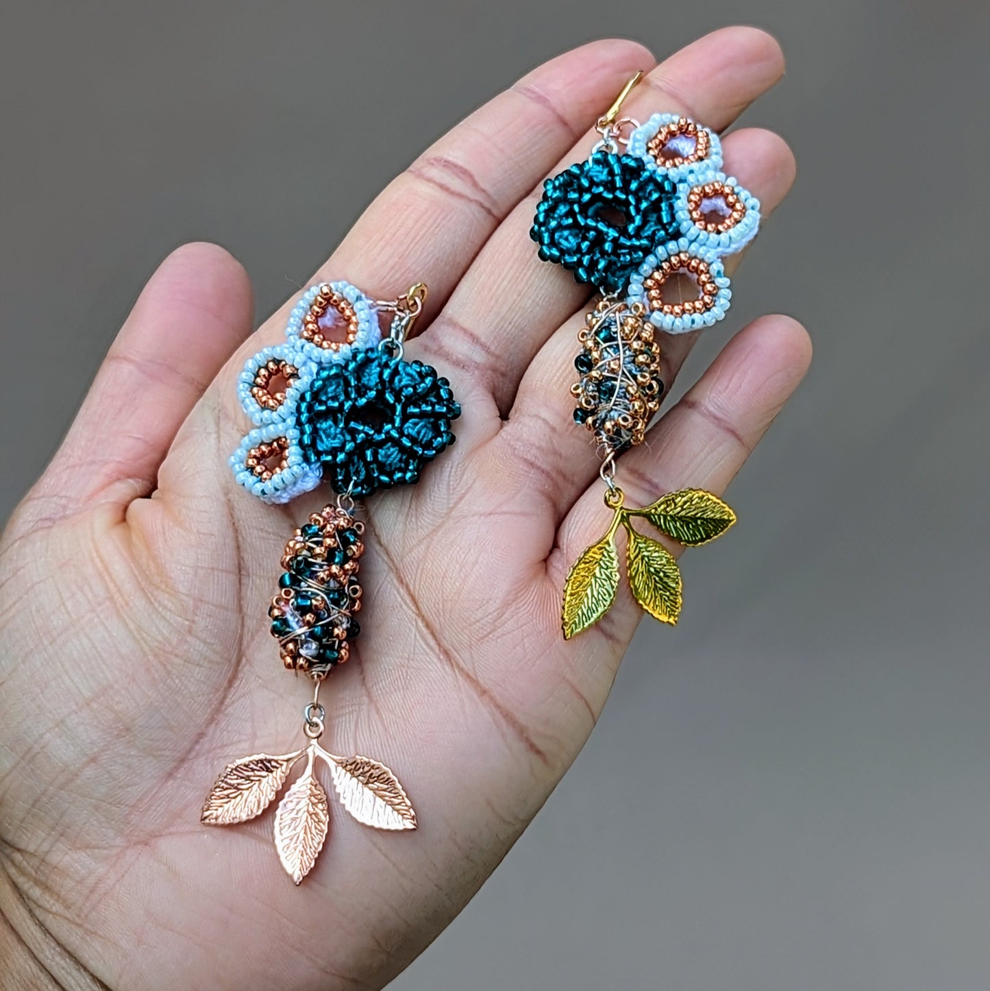 Asymmetric earrings by Mayaani Jewellery featuring a striking seahorse motif. Crafted from white and rose gold with turquoise accents, these earrings highlight intricate hand-crocheted elements and copper details. The vibrant combination of white and emerald green seed beads, paired with cascading gold and rose gold plated leaves, evokes organic shapes. Made from recycled materials, these sustainable earrings are ideal for weddings and special occasions, symbolizing growth and renewal.