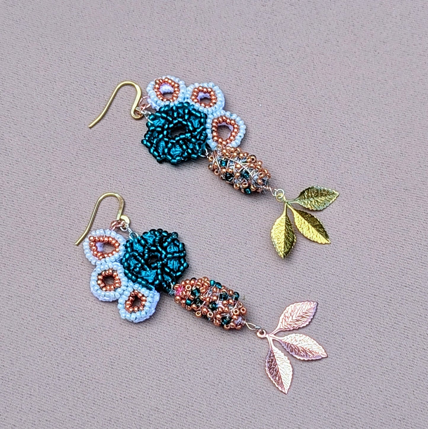 Exquisite asymmetric earrings by Mayaani Jewellery, inspired by seahorse motifs. Crafted from white and rose gold with turquoise accents, these earrings feature hand-crocheted elements and copper highlights. The design includes a lively mix of white and emerald green seed beads, enhanced by cascading gold and rose gold plated leaves. Made with recycled materials, they embody sustainability, making them a perfect choice for special occasions and symbolizing growth and renewal.