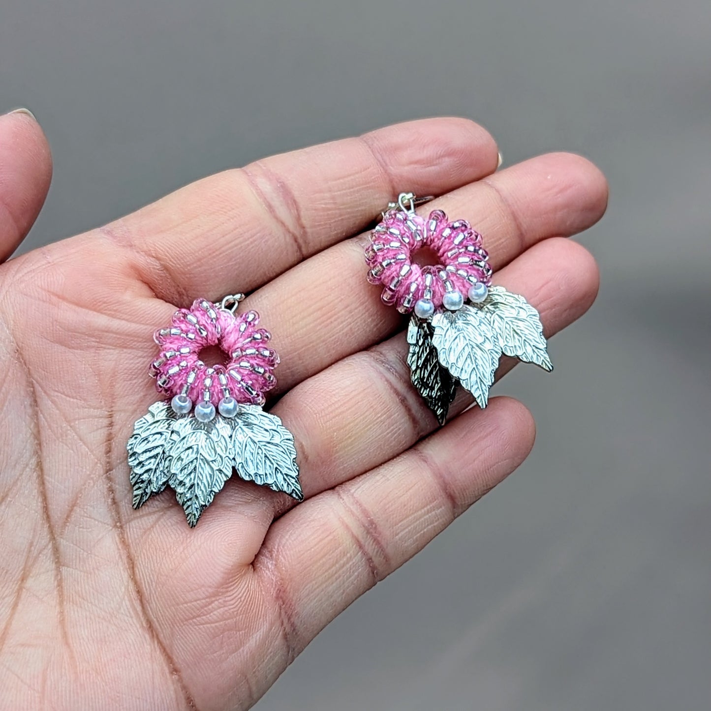 Elegant handcrafted earrings by UK-based sustainable brand Mayaani Jewellery, featuring a baby pink beaded floral design accented with seed pearls, complemented by three finely detailed silver leaves dangling below. The design reflects a blend of nature-inspired elements and artisan craftsmanship.