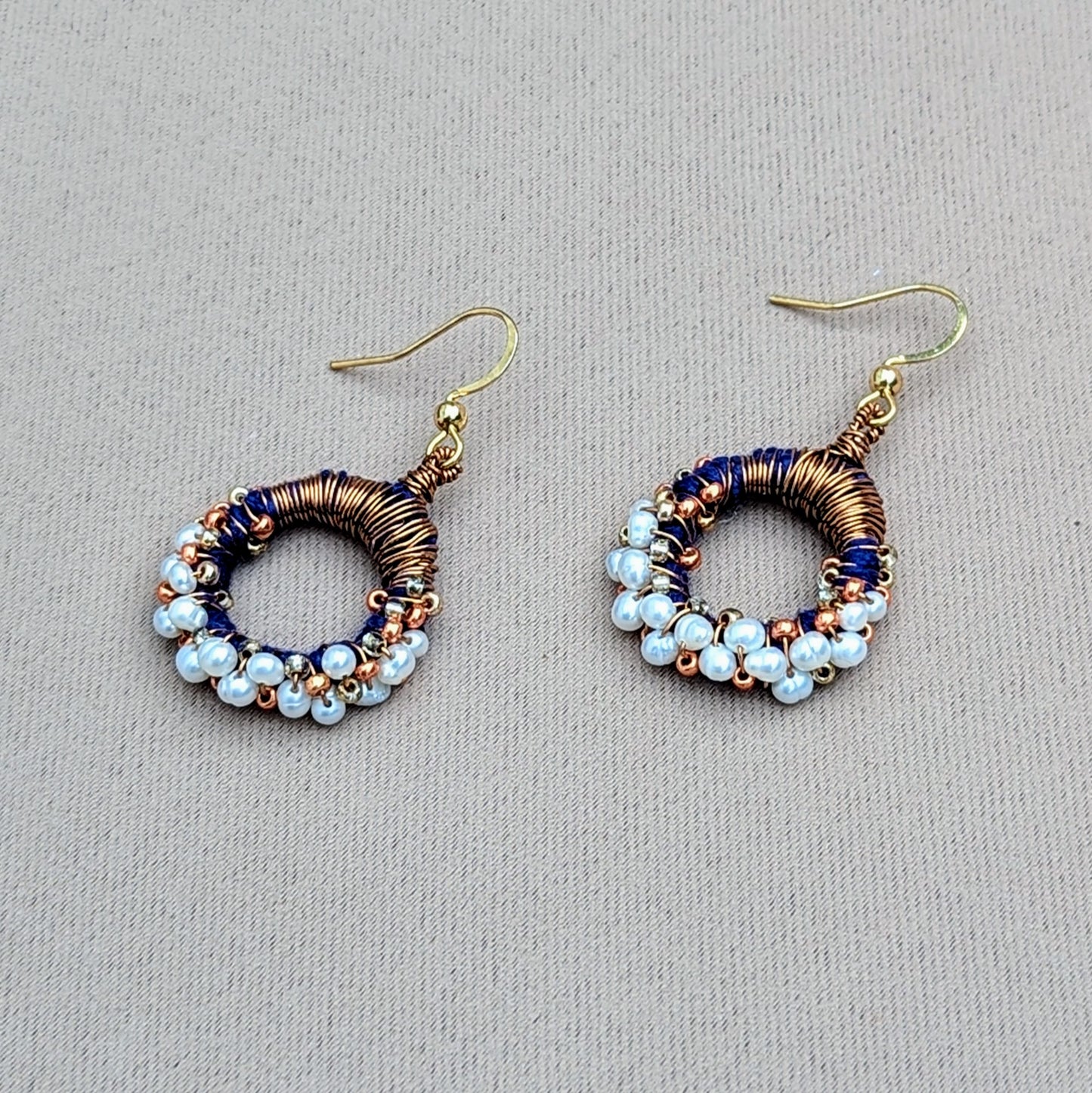 These contemporary Indian-style earrings offer a fresh take on traditional pearl jewellery exclusive to sustainable UK brand Mayaani Jewellery. Combining royal blue hand-crocheted thread work with skilful antique bronze copper wire wrapping they are accented with rose gold and gold beads. The earrings also feature a border of lustrous ivory freshwater pearls for a striking yet sophisticated contrast. Embrace the elegance of pearls with a modern ethnic touch.