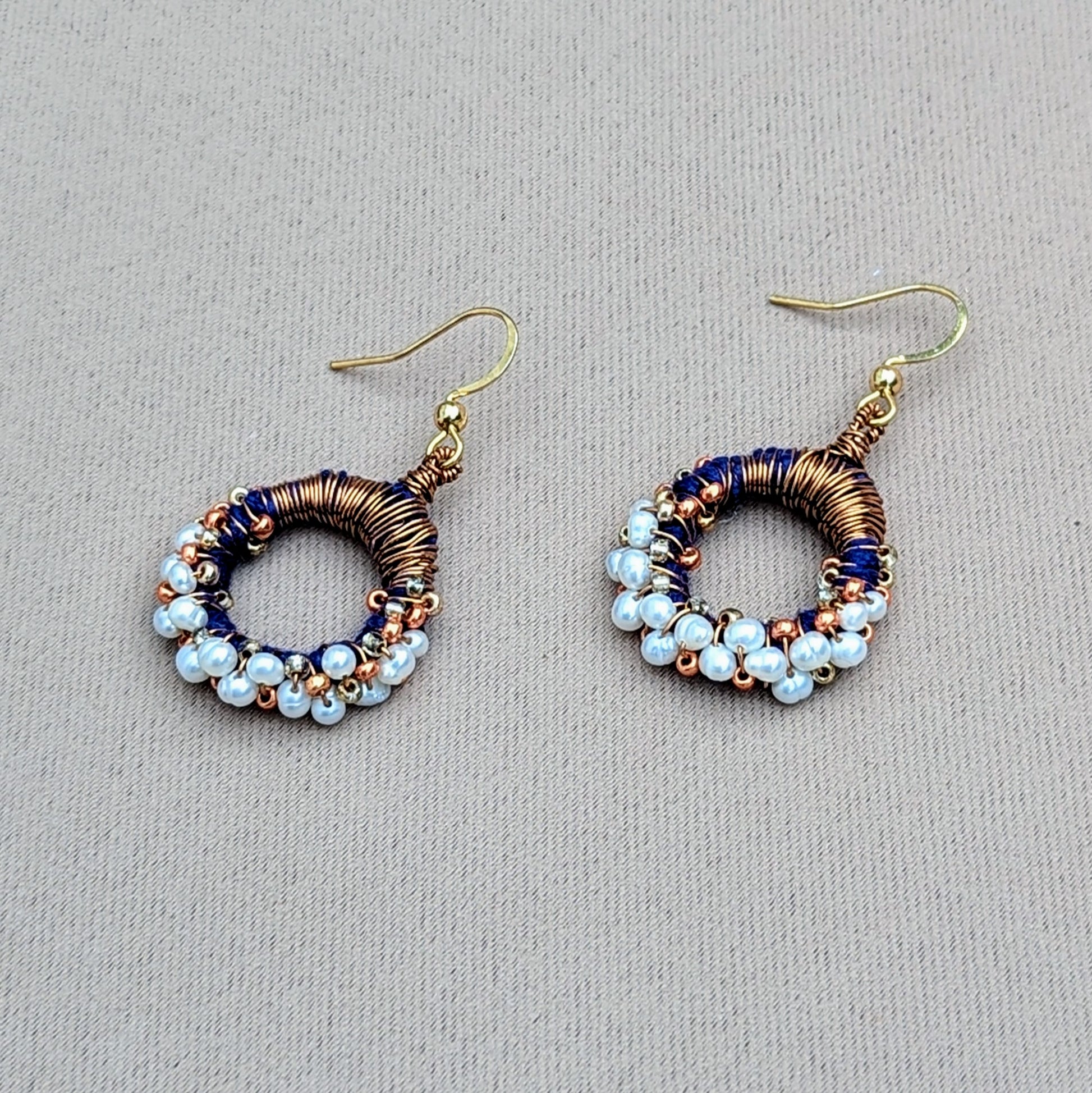 These contemporary Indian-style earrings offer a fresh take on traditional pearl jewellery exclusive to sustainable UK brand Mayaani Jewellery. Combining royal blue hand-crocheted thread work with skilful antique bronze copper wire wrapping they are accented with rose gold and gold beads. The earrings also feature a border of lustrous ivory freshwater pearls for a striking yet sophisticated contrast. Embrace the elegance of pearls with a modern ethnic touch.