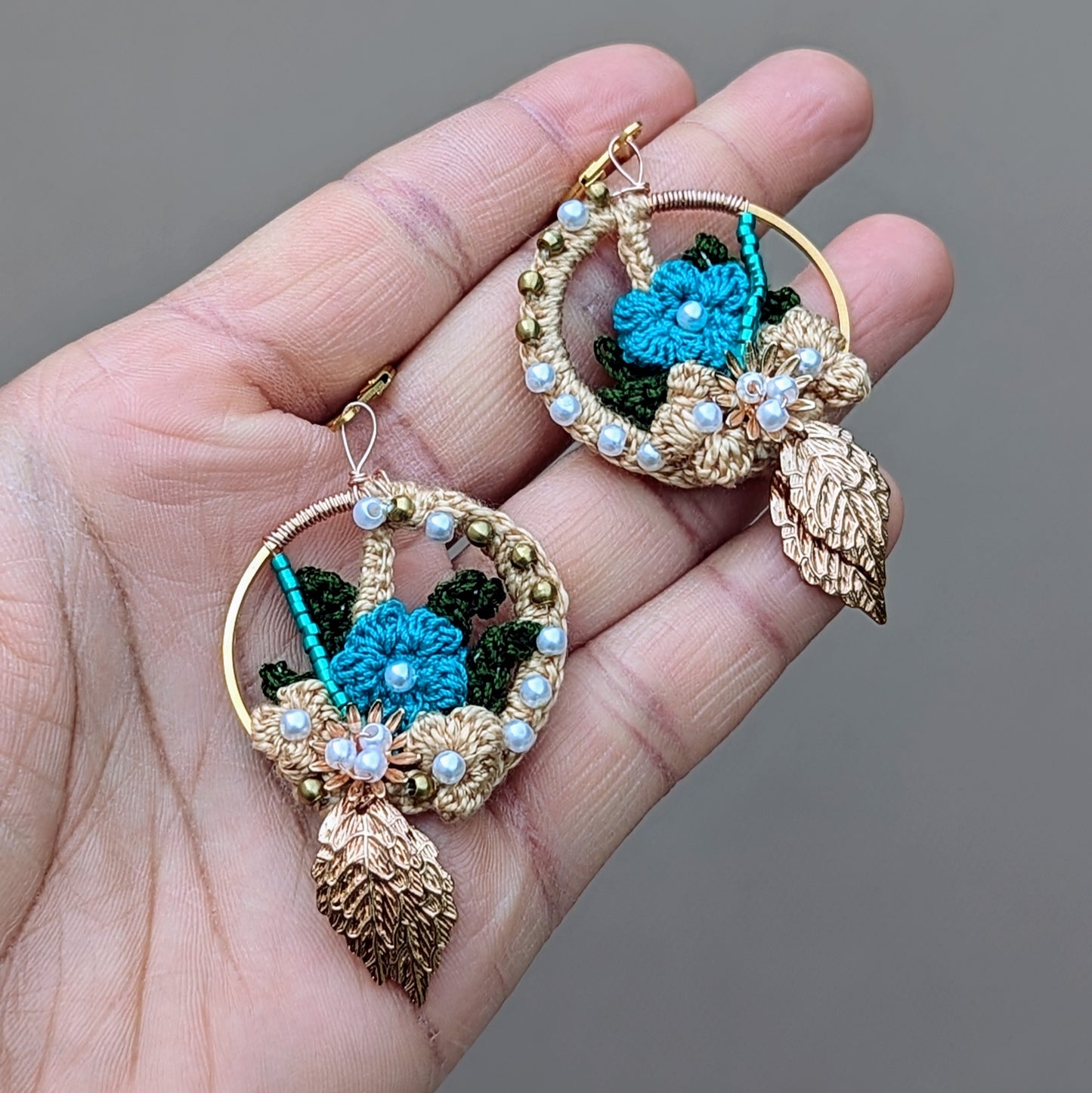 Discover the artistry of these handcrafted Indian-inspired earrings, pictured in the palm of a hand, exclusively from Mayaani Jewellery, a sustainable UK brand. They feature a stunning combination of solid brass, seed pearls, and blue beads, highlighted by gold, blue, and dark green crochet floral designs. Lightweight and comfortable, these earrings are perfect for everything from weddings and special events to everyday style.