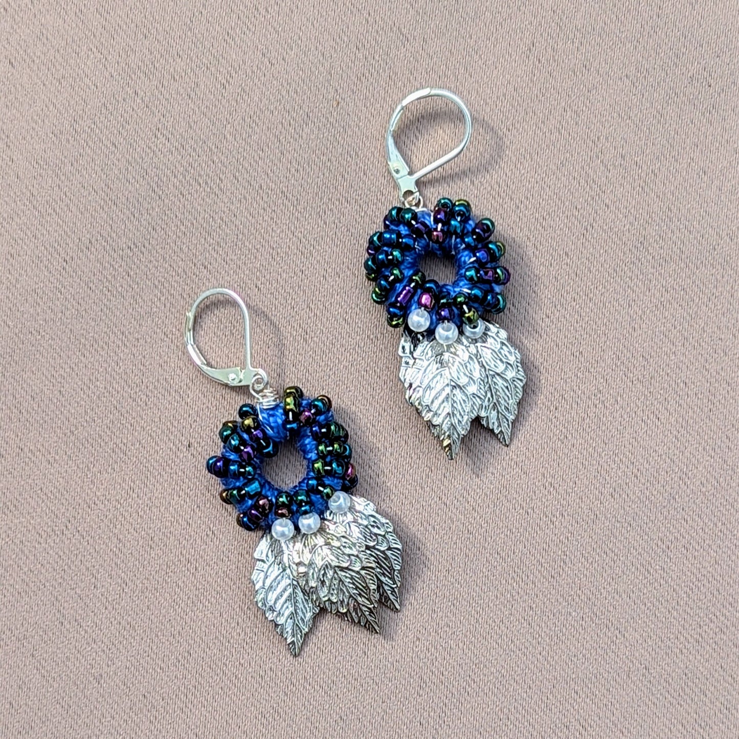 A unique pair of artisan handcrafted Indian style earrings by sustainable UK brand Mayaani Jewellery featuring a circular blue bead design with ivory seed pearl and silver leaf accents. A sumptuous blend of hand crochet, hand bead work and hand wire wrapping finished off with 925 stamped lever back hooks for contemporary style with expert traditional artistic craftsmanship.