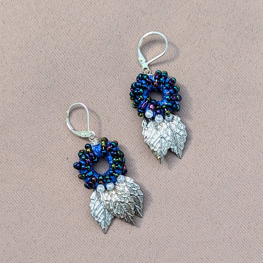 A unique pair of artisan handcrafted Indian style earrings by sustainable UK brand Mayaani Jewellery featuring a circular blue bead design with ivory seed pearl and silver leaf accents. A sumptuous blend of hand crochet, hand bead work and hand wire wrapping finished off with 925 stamped lever back hooks for contemporary style with expert traditional artistic craftsmanship.