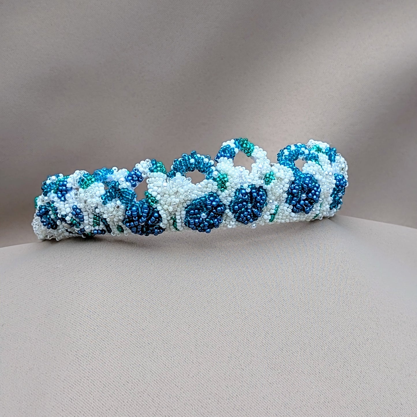 This distinctive handcrafted bridal tiara in blue, white, and silver, along with matching earrings, is offered by the sustainable UK brand Mayaani Jewellery. Inspired by the colors of the ocean, this vintage-style piece showcases delicate white hand crochet and beaded floral designs using deep blue and turquoise seed beads, plus seed pearls. Wear it as a headband for a lovely "something blue" accent in your bridal attire.