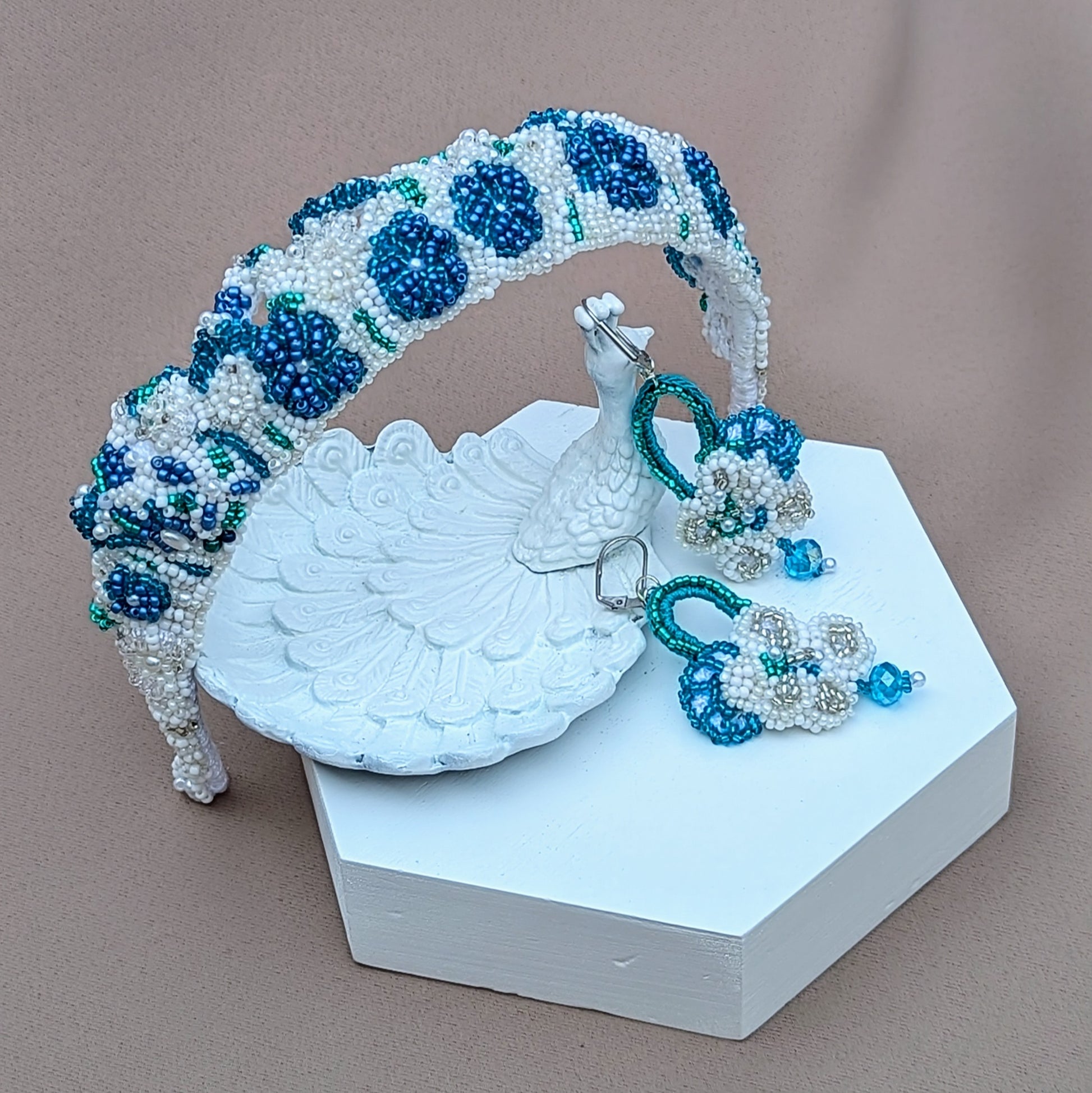 Discover this one-of-a-kind handcrafted bridal tiara in blue, white, and silver, accompanied by matching earrings from sustainable UK brand Mayaani Jewellery. Inspired by the colors of the ocean, this vintage-style piece features detailed hand crochet and floral motifs. Versatile enough to be worn as a headband, it adds a lovely "something blue" element to your bridal attire. The statement earrings, made with high-quality upcycled Swarovski bicone beads, can also act as your "something borrowed!"