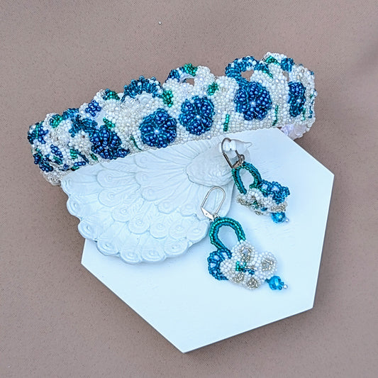 A one-of-a-kind handcrafted bridal tiara in blue, white, and silver, paired with matching earrings from sustainable UK brand Mayaani Jewellery. Inspired by ocean hues, this vintage-style piece features intricate hand crochet and hand beaded floral motifs. Versatile enough to be worn as a headband, it adds a charming touch of "something blue" to your bridal look with the statement earrings, featuring high quality upcycled Swarovski bicone beads, doubling up as your something borrowed!