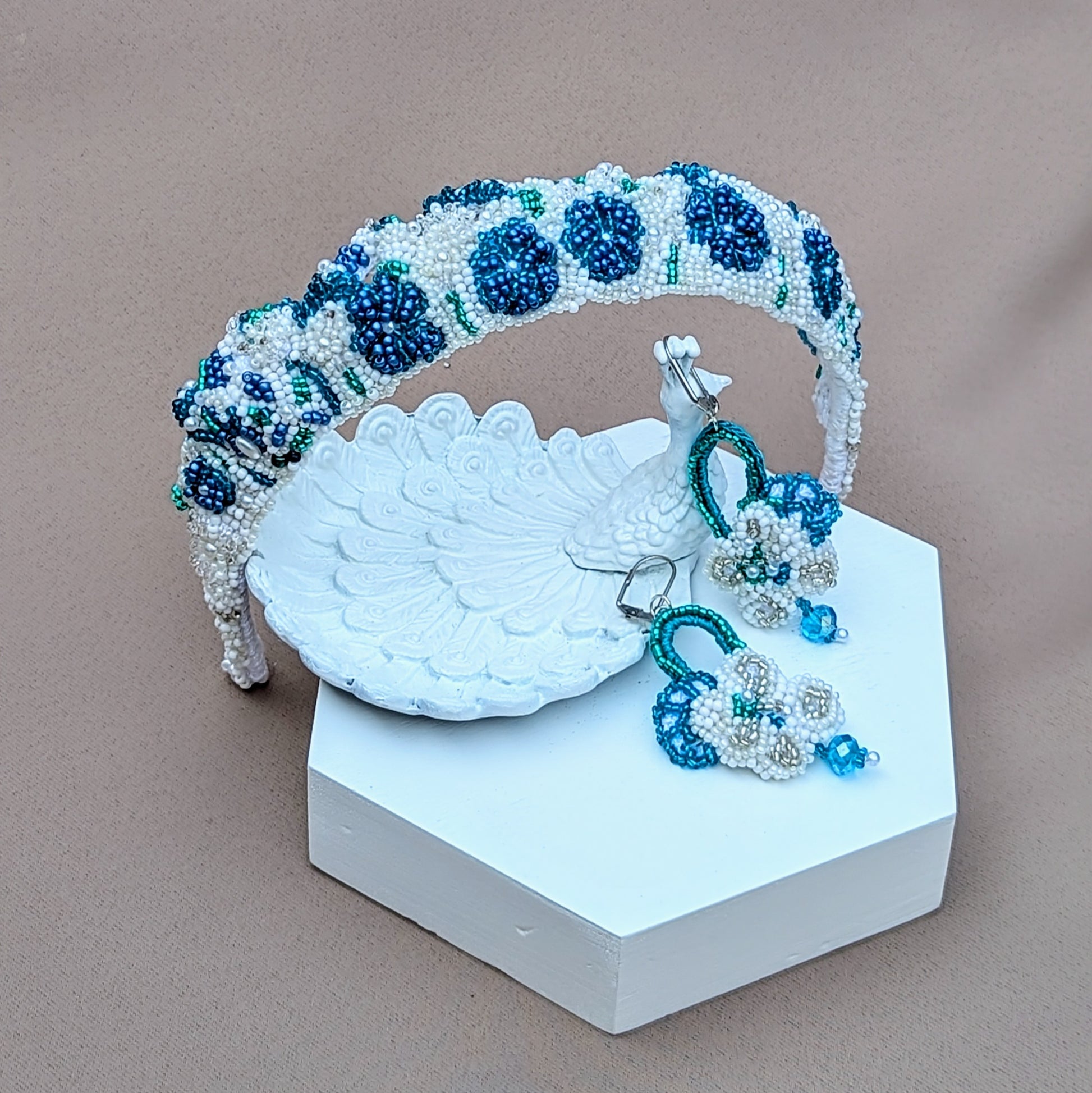 This unique handcrafted bridal tiara in blue, white, and silver, complete with matching earrings from sustainable UK brand Mayaani Jewellery, is inspired by ocean shades. This vintage-style piece showcases intricate hand crochet and beaded floral designs. Wear it as a headband for a charming "something blue" accent in your bridal ensemble. The statement earrings, featuring high-quality upcycled Swarovski bicone beads, also serve as your "something borrowed!"