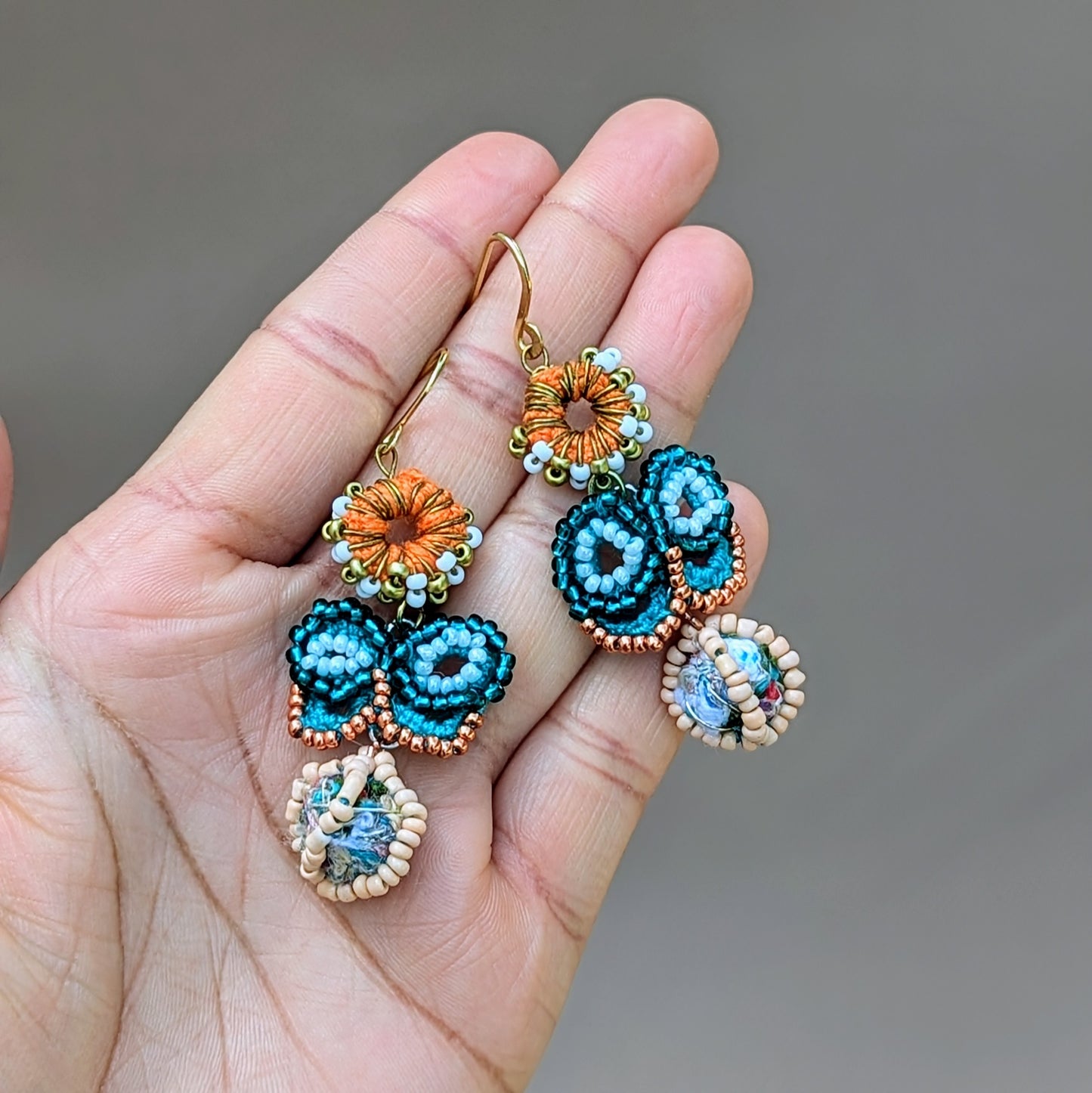 Handcrafted eco-friendly blue butterfly earrings from sustainable brand Mayaani Jewellery UK. The design showcases a turquoise and rose gold seed bead butterfly atop an orange crochet circle, embellished with white and gold seed beads, and finished with sturdy gold-plated stainless steel hooks. Transform your style in an instant in this statement worthy pair.