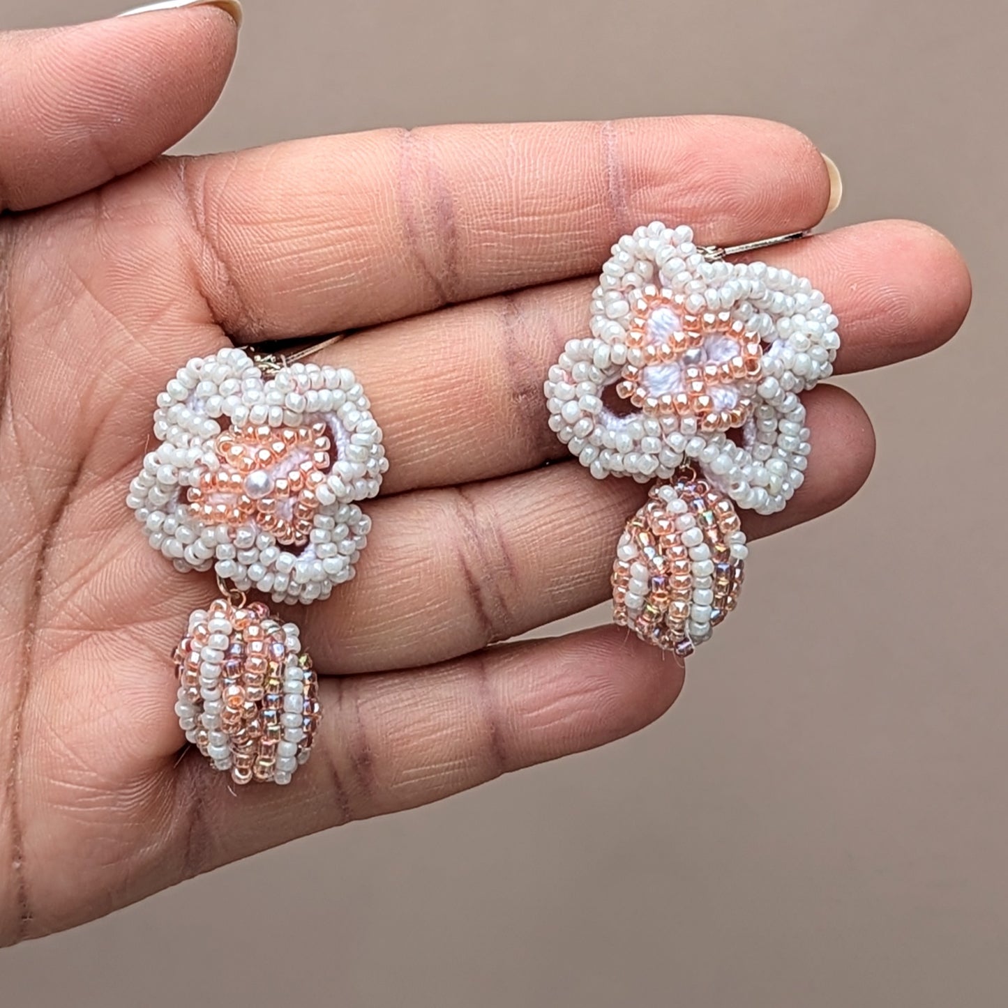 Elegant white and peach bead crochet earrings that combine bridal tradition of 'something borrowed' with sustainable craftsmanship exclusively designed for Mayaani Jewellery UK. Each earring features a scrap bead sourced from leftover materials, elegantly placed at the base of a hand-crocheted floral design. Completed with luxurious 925 stamped sterling silver lever back hooks, these unique earrings celebrate eco-friendly artistry with luxurious fashion forward style.