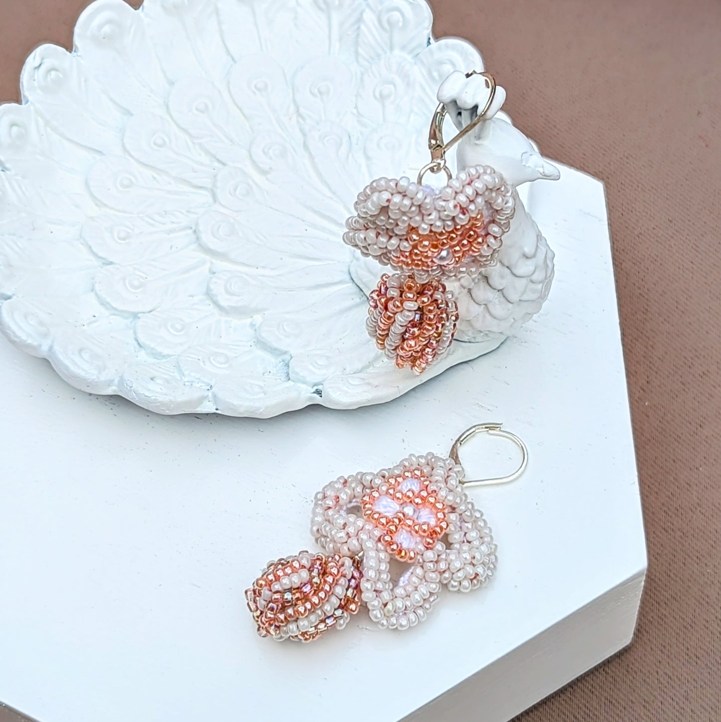 These stunning white and peach bead crochet earrings blend bridal traditions of 'something borrowed' with sustainable artistry exclusive to Mayaani Jewellery UK. Each earring features a scrap bead created from our designer's waste materials, elegantly set beneath a hand-crocheted floral motif. Completed with 925 stamped sterling silver lever back hooks, they embody unique, eco-friendly design.