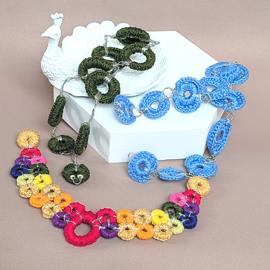 This image displays a unique one of a kind necklace made by Mayaani Jewellery, sustainable UK brand, featuring handcrafted circular crochet and wire wrapped chain links in a variety of colours including greens, blues, and a vibrant rainbow section. The piece has a clasp-free finish, allowing for versatile wear, and includes interchangeable chains for customisation. The crochet-style design and attention to detail showcase the brand's commitment to sustainability and artisanal craftmanship.