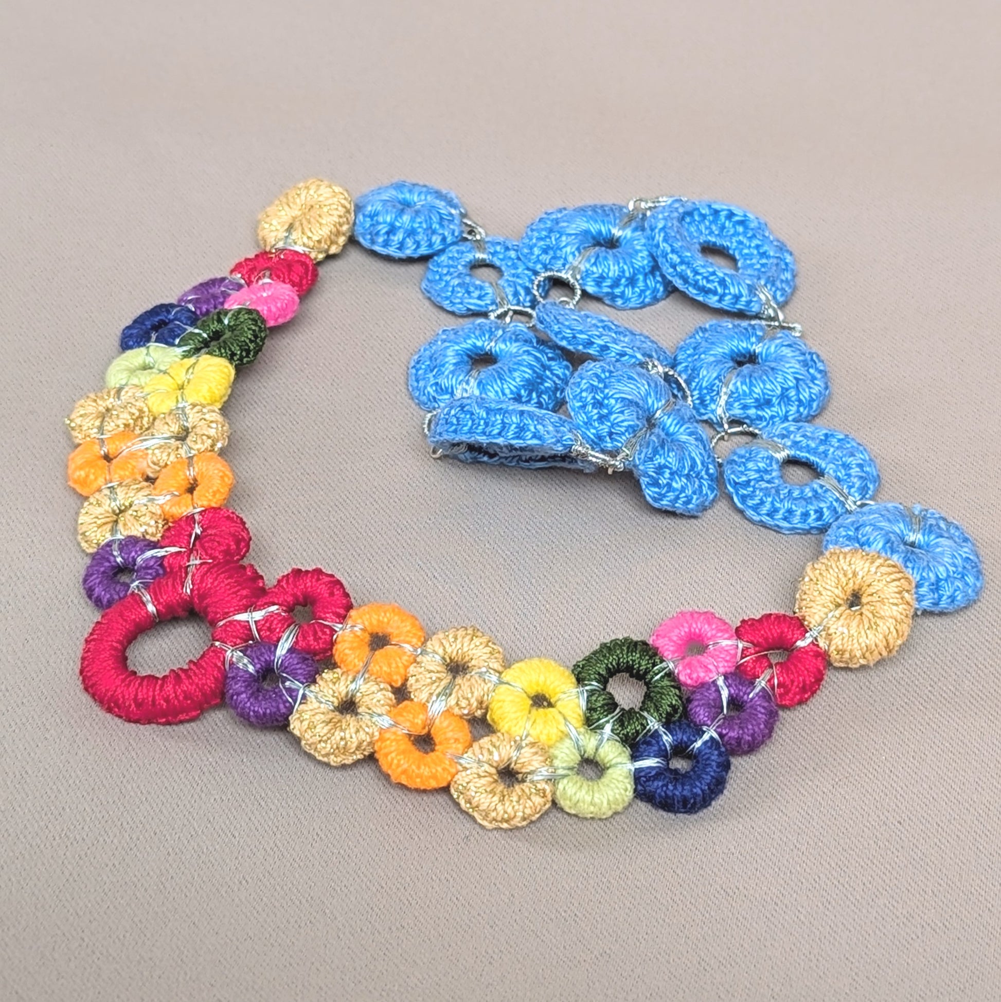 A distinctive clasp free multicoloured necklace by sustainable brand Mayaani Jewellery UK featuring colourful crochet rings and a rainbow palette. This handmade design pictured with a classic denim blue crochet chain, offers interchangeable chains, allowing the wearer to customise it to their liking. 