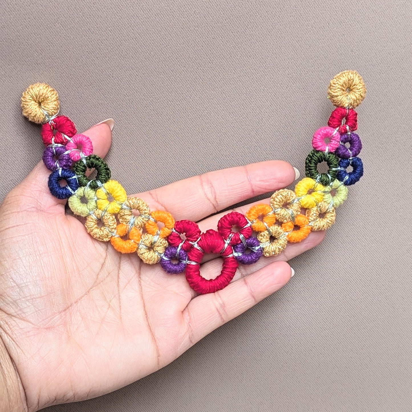 This image highlights a unique necklace from the sustainable UK brand Mayaani Jewellery featuring handcrafted crochet links in a variety of shades which together create a vibrant rainbow. The necklace has no clasp offering a sleek, comfortable fit and it features interchangeable chains which can be fully customised to your preferences.