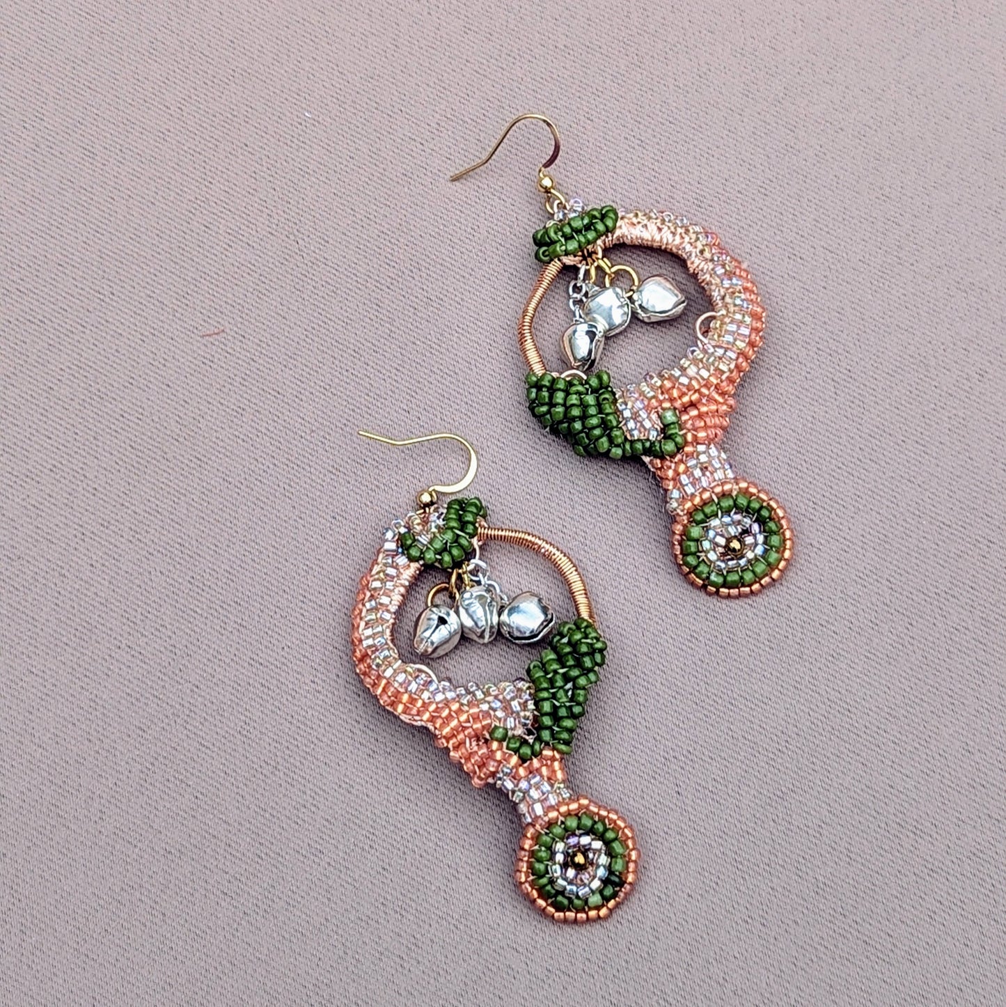 A pair of lightweight, Indian-inspired earrings by the sustainable UK brand Mayaani Jewellery. These goddess-worthy earrings, designed to bring out the dancer in you, are adorned with solid silver ghungroo bells that produce a melodious chime with each movement, celebrating your classical Indian dance roots. With luxurious silver, peach, and green beads, along with intricate hand crochet and wire wrapping, they are an ideal choice for weddings and special occasions.