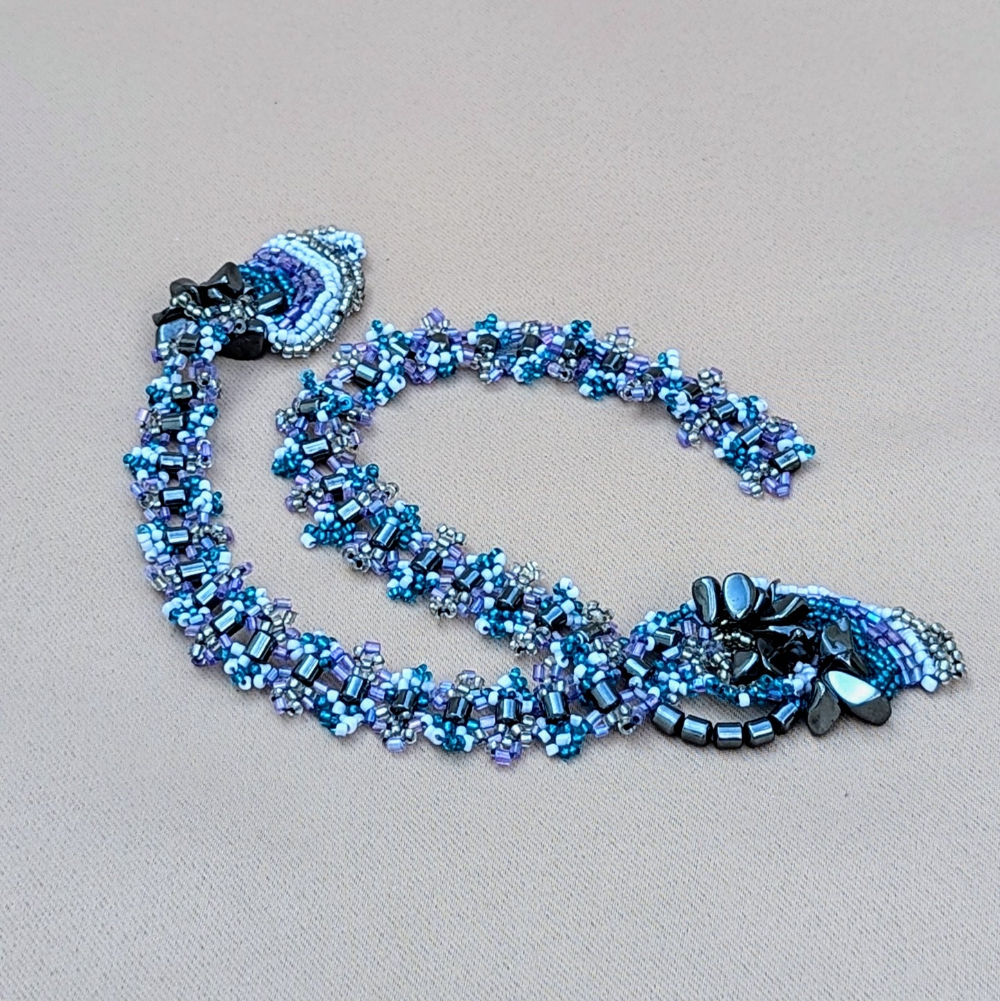 A striking necklace from sustainable brand Mayaani Jewellery UK, featuring luxurious upcycled hematite beads intricately woven with premium seed beads in lilac, blue, white, and silver. This versatile piece is perfect for weddings and daily wear, symbolizing strength and beauty. A custom clasp will be fitted before shipping, with selection options sent via email.