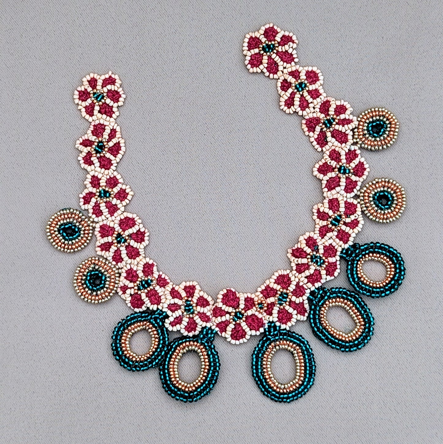 One-of-a-kind Indian-inspired handmade necklace exclusive to sustainable UK brand Mayaani Jewellery featuring intricate hand crochet, hand beadwork and wirework. The design showcases red, emerald green and peach tones with rose gold and gold accents creating a modern take on traditional Indian bridal colours. The necklace has floral patterns with dangling circular bead elements, giving it an elegant, timeless appeal.