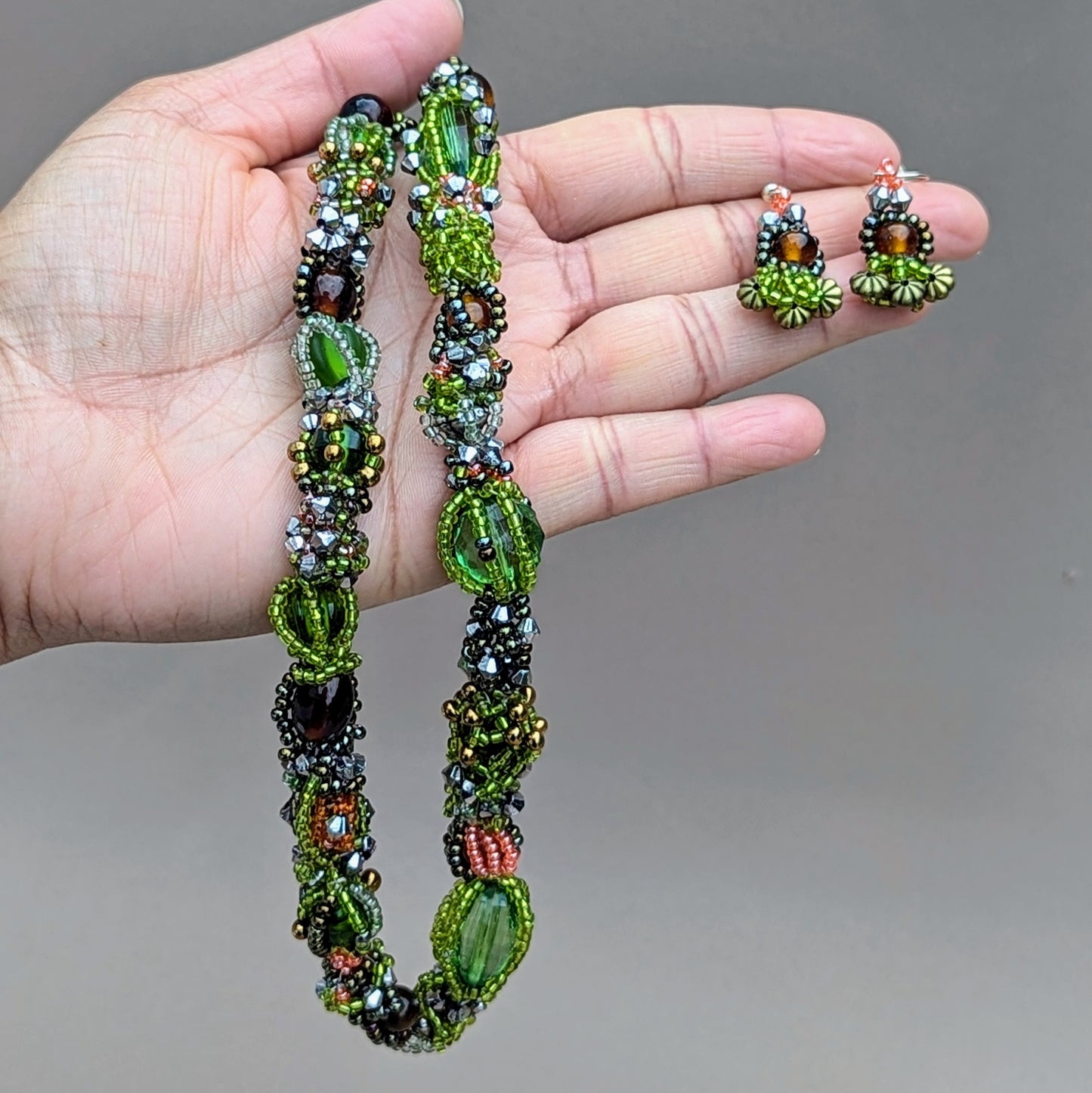 Step into a vibrant garden of greens and browns that honors the beauty of nature's seasons with this unique artisan handcrafted beaded choker necklace from sustainable Indian UK brand Mayaani Jewellery. Showcasing a mix of new and premium upcycled glass seed beads, this statement piece is intricately woven and artistically crafted, making it the perfect accessory for the modern eco-conscious woman. It is accompanied by a matching pair of short drop earrings.