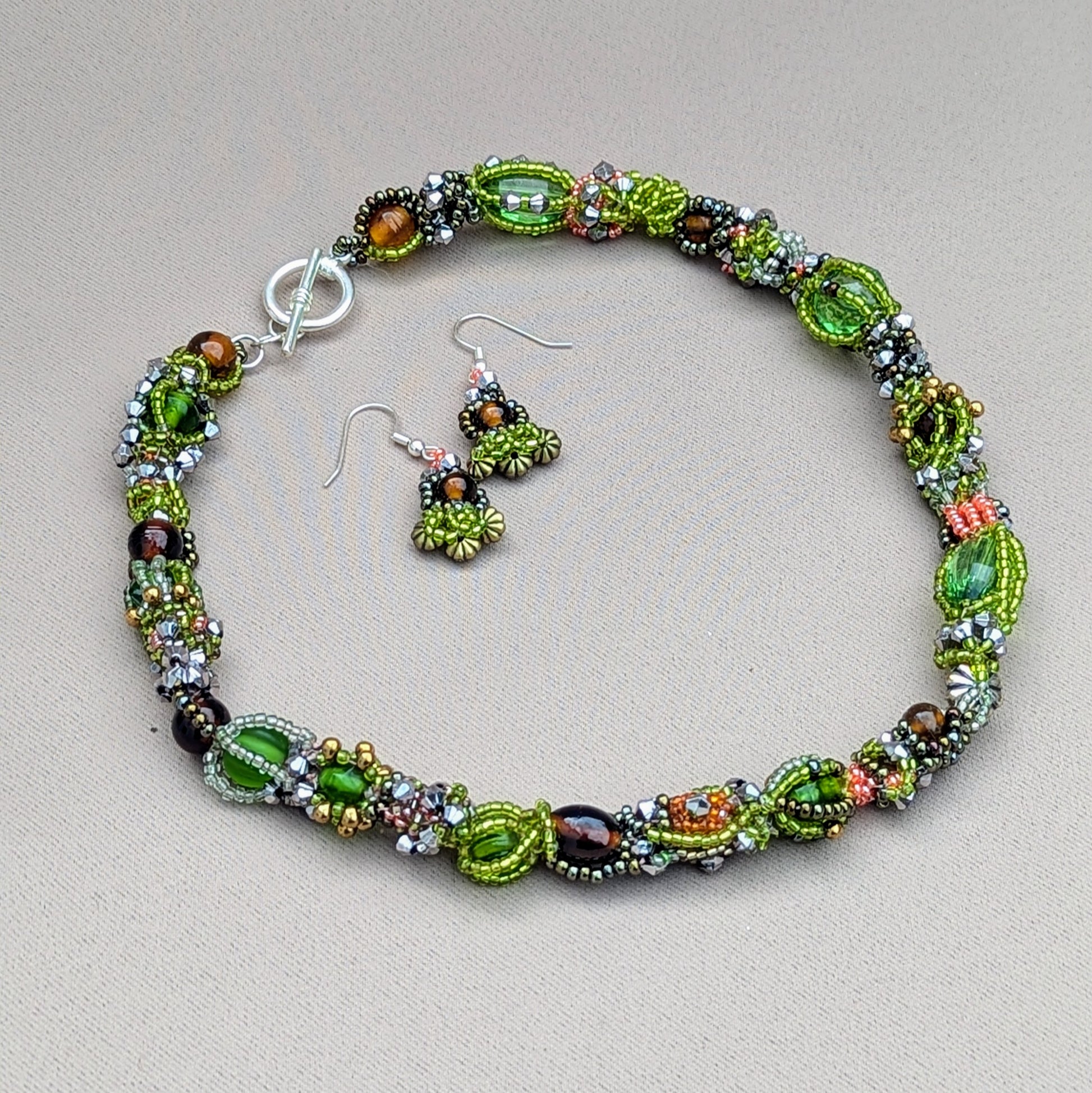 Immerse yourself in a bold beautiful garden of greens and browns celebrating natures many seasons with this unique artisan handcrafted beaded choker style necklace by sustainable Indian UK brand Mayaani Jewellery. Featuring a mixture of new and high quality upcycled glass seed beads expertly woven and artistically intertwined this sustainable statement piece is perfect for any outfit and comes with a pair of complementary short drop earrings.