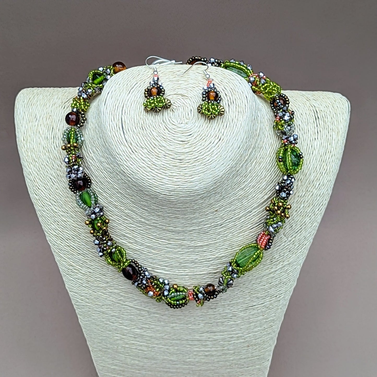 Dive into a stunning garden of greens and browns that celebrates nature’s diverse seasons with this unique artisan handcrafted beaded choker necklace from sustainable Indian UK brand Mayaani Jewellery. Displayed on an elegant hemp bust, this striking piece features a blend of new and high-quality upcycled glass seed beads, expertly woven and artistically intertwined. It’s perfect for enhancing any outfit with sustainable fashion forward style and comes with a matching pair of short drop earrings.