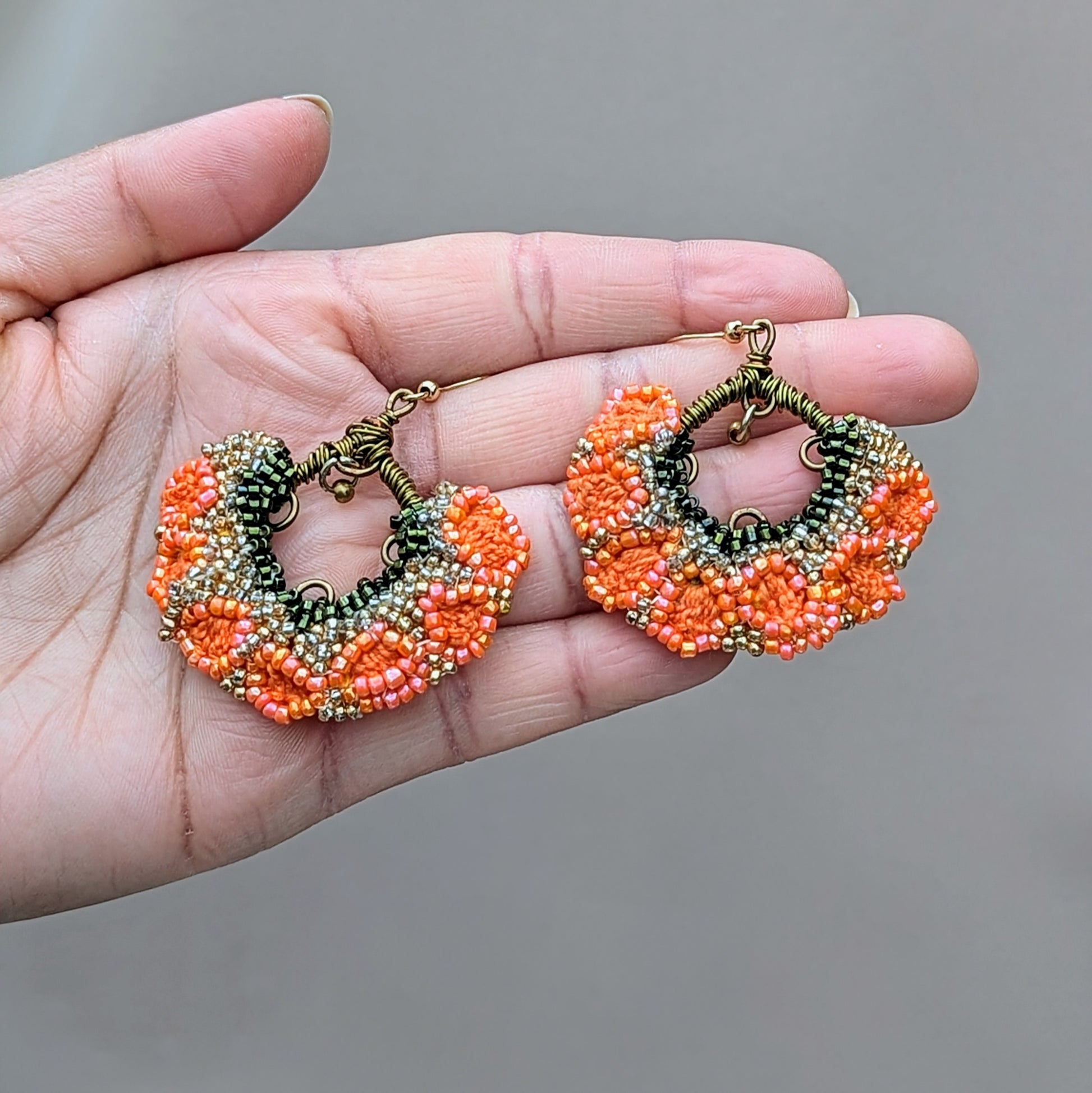 Elevate your Indian style with this striking pair of orange, green, and gold earrings, exclusively from Mayaani Jewellery, a sustainable UK brand. Featuring a charming brass bead that dangles gracefully from hand-wrapped bronze copper wire, these earrings create a lively movement within their floral fan-like shape. They are a joyful addition for both special occasions and everyday life.