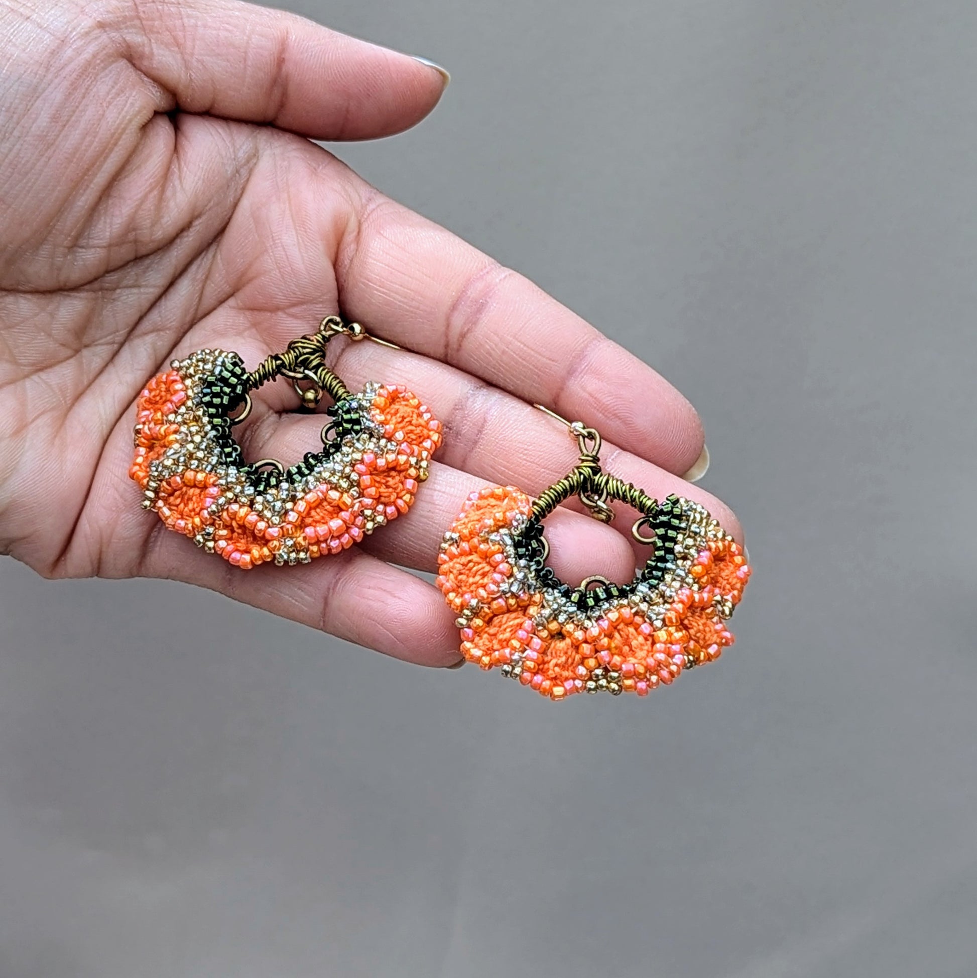 Introducing a beautiful pair of Indian style earrings in vibrant orange, green, and gold, exclusive to Mayaani Jewellery, a sustainable UK brand. Featuring a small brass bead that gracefully dangles from hand-wrapped bronze copper wire, these earrings create a playful movement in the floral fan design. They bring pure joy for both special occasions and your everyday outfits.