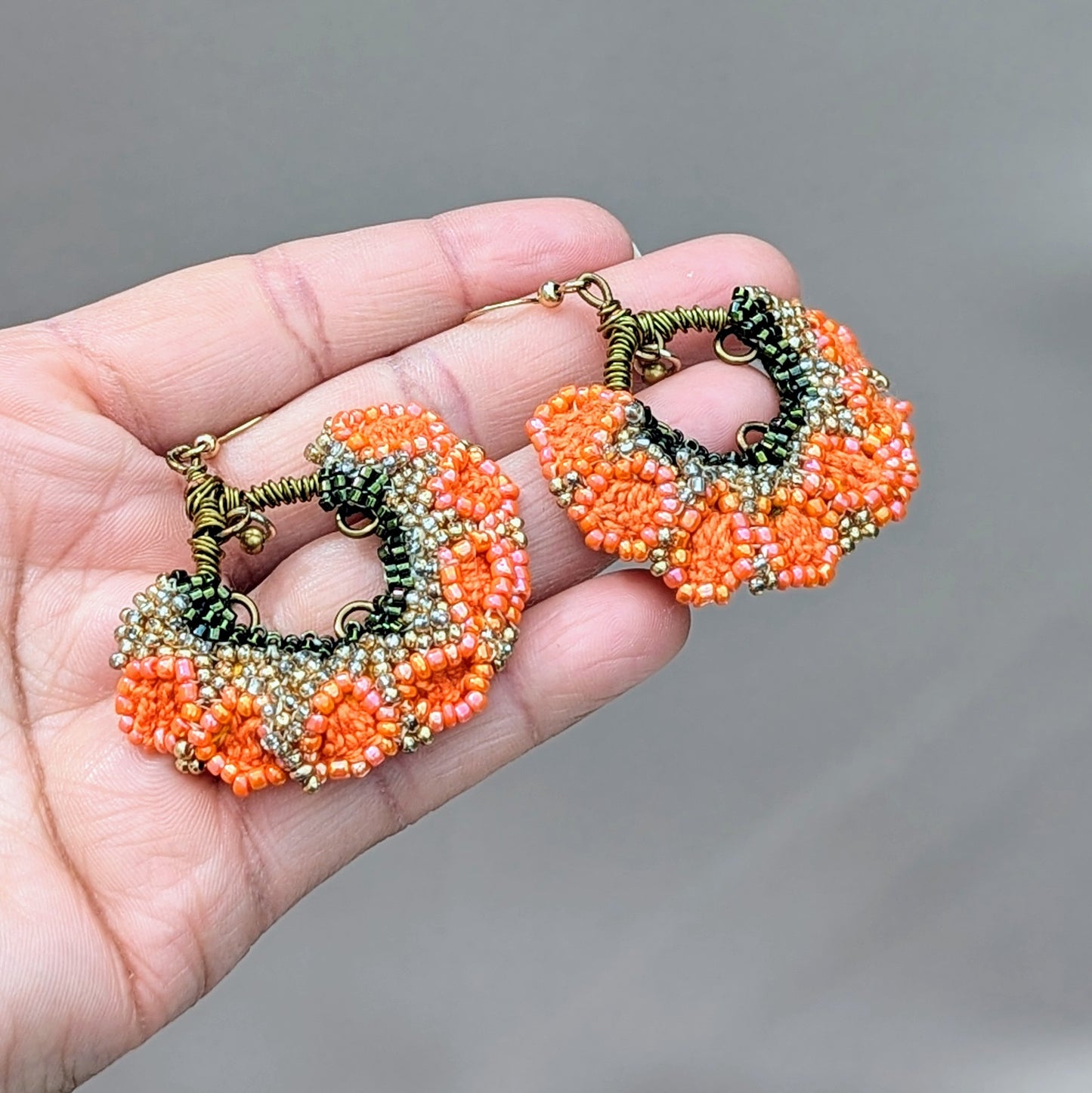 Introducing a stunning pair of Indian inspired earrings in bold orange, green, and gold, exclusive to the sustainable UK brand Mayaani Jewellery. These earrings feature a charming brass bead that delicately dangles from intricately wrapped bronze copper wire, adding delightful movement to the floral fan-like design. Perfect for special occasions or everyday wear, they bring a touch of joy to any outfit.