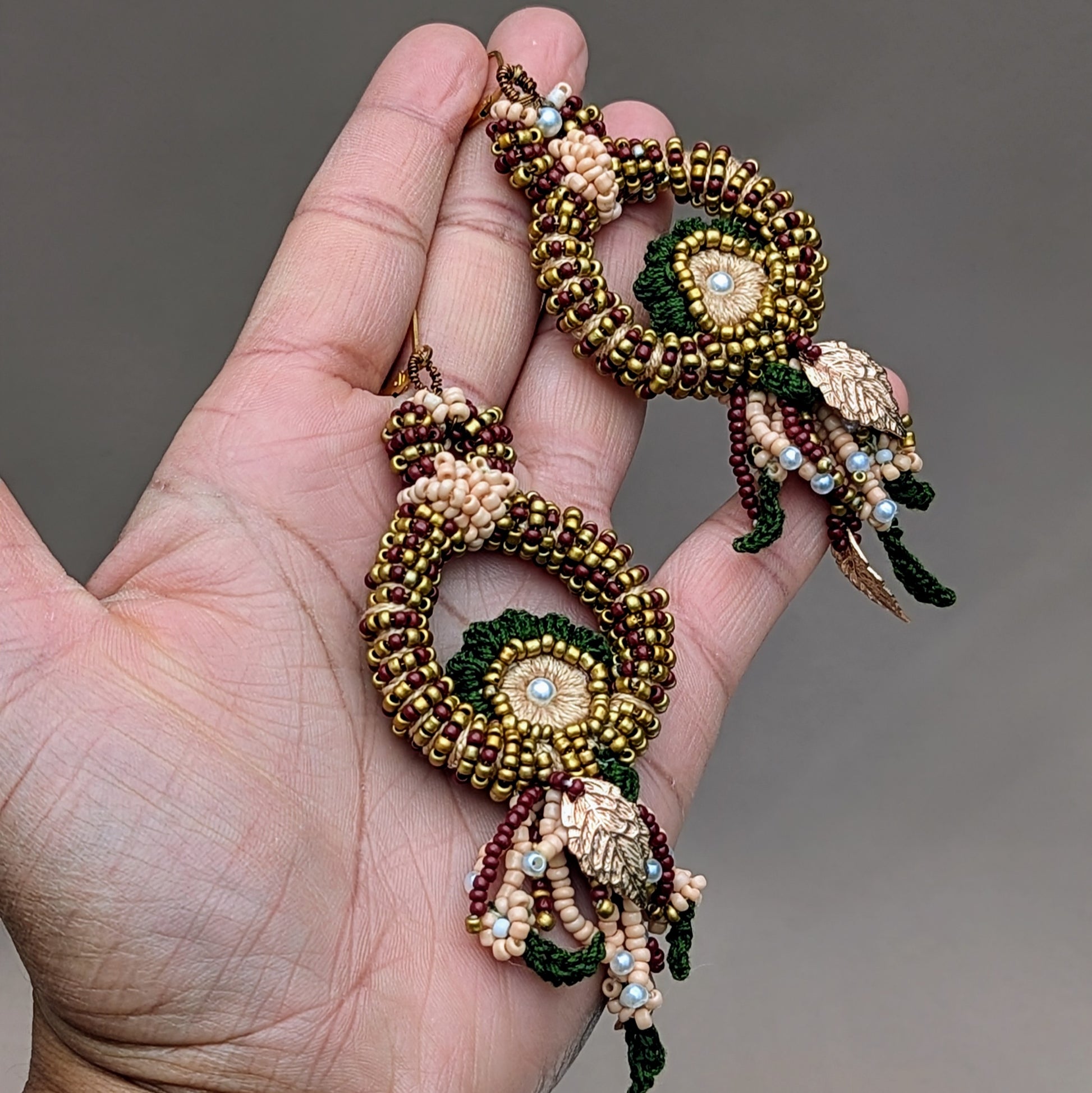 Introducing a unique pair of artisan handcrafted Indian bridal earrings by Mayaani Jewellery, a sustainable UK brand. These eye-catching earrings feature rich red, green, and gold tones, elegantly shaped like a peacock. Crafted with intricate bead embroidery, hand crochet, and precise wire wrapping, they embody exceptional quality and artistry.