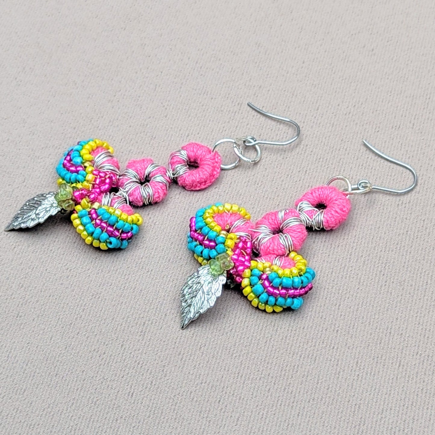 These one-of-a-kind, Indian-inspired earrings from Mayaani Jewellery, a UK-based sustainable brand, feature bright pink crochet accents, vibrant beadwork in turquoise, yellow, and purple with elegant silver leaf charms. Made from high quality upcycled materials, including peridot gemstone chips, these earrings are lightweight, comfortable, and showcase Mayaani's commitment to sustainable luxury and artistic craftmanship.