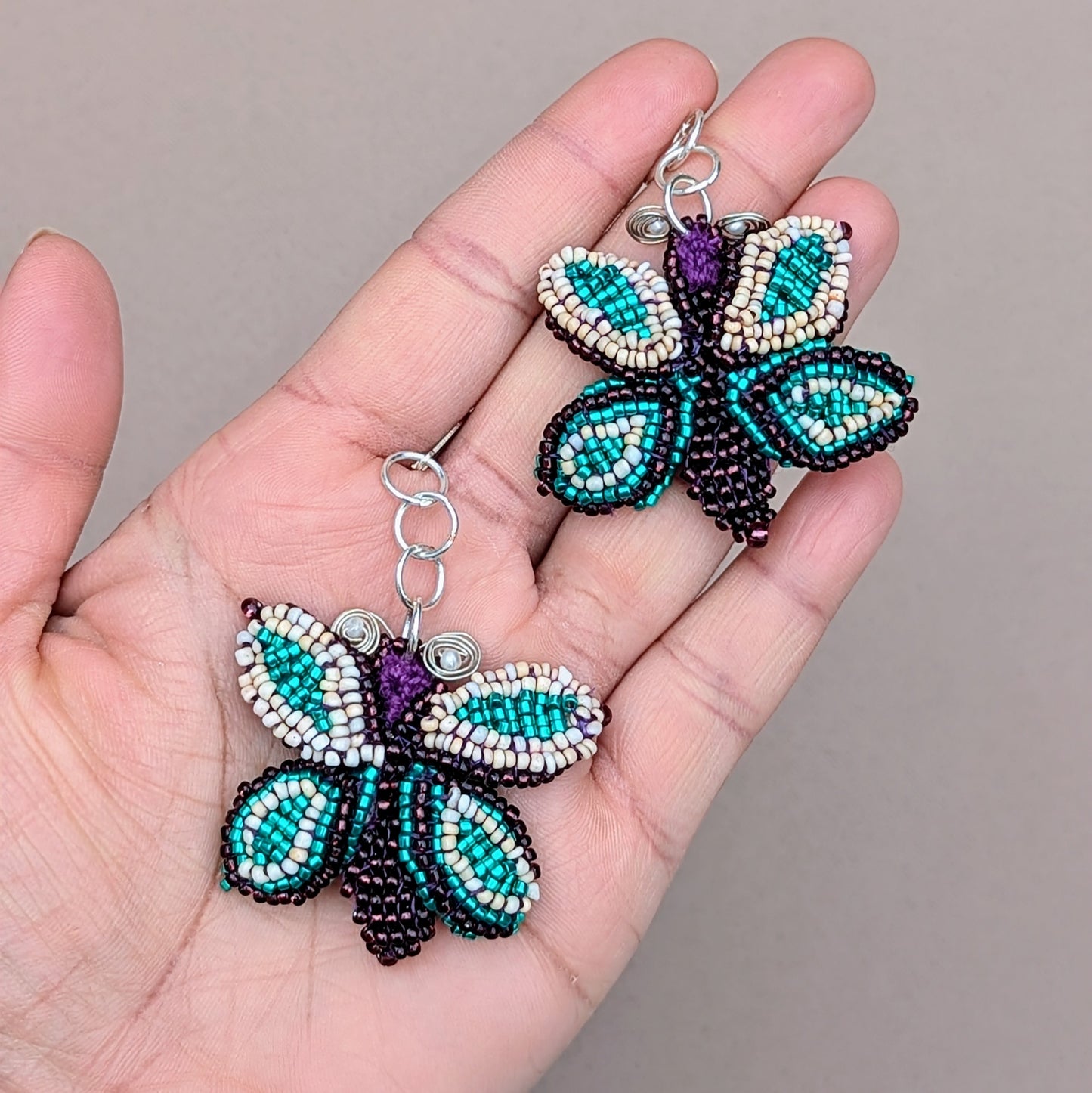 A stunning pair of artisan handcrafted butterfly statement earrings, exclusively from the sustainable UK brand Mayaani Jewellery, Featuring intricate beadwork over a hand-crocheted base, complemented by delicate wire wrapping and finished with 925 stamped sterling silver lever-back hooks. The beautiful combination of purple, soft peach and vibrant turquoise ensures this pair makes a striking statement for any occasion including everyday.