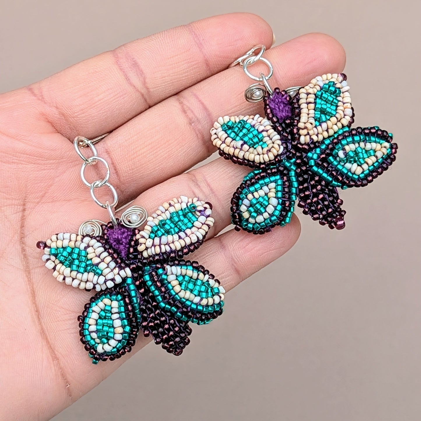 Mayaani Jewellery presents an exclusive pair of artisan handcrafted butterfly statement earrings, featuring intricate beadwork atop hand-crochet detailing. The design is finished with hand wire-wrapping accents and 925 stamped sterling silver lever-back hooks. The vibrant mix of purple, creamy peach, and bright turquoise makes these earrings an eye-catching accessory for every occasion including everyday.