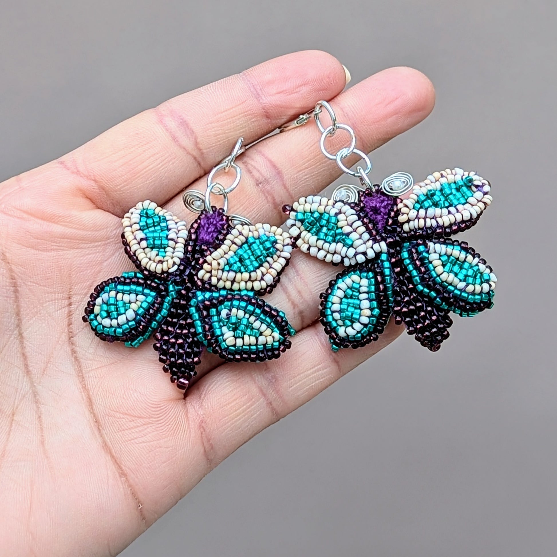 A unique pair of butterfly statement earrings, handcrafted by Mayaani Jewellery, a sustainable UK brand. This design features exquisite beadwork set against a hand-crocheted backdrop, enhances with delicate wire-wrapped accents. The 925 stamped sterling silver lever-back hooks and the bold colour combination of purple, peach and turquoise ensure these earrings make a beautiful statement.