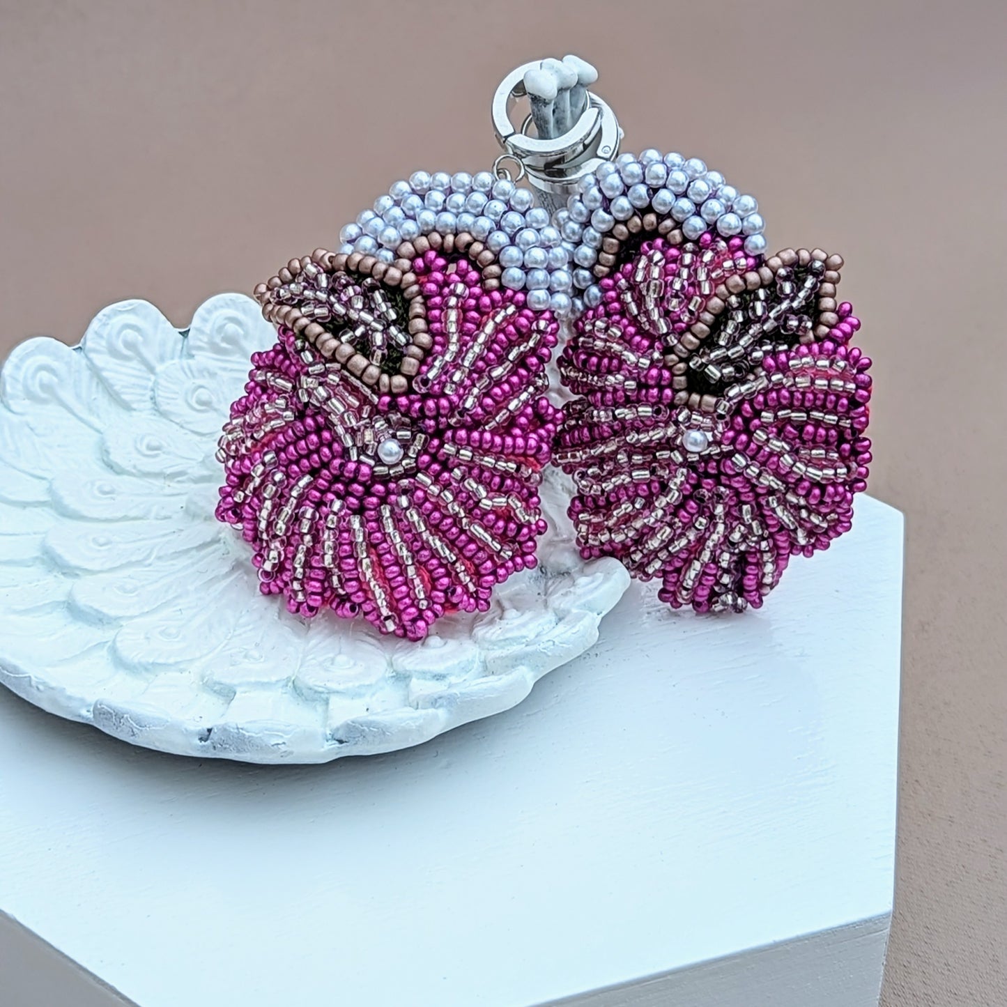 A unique one of a kind bold statement pair of purple white and silver earrings exclusively from Mayaani Jewellery displayed on a white peacock trinket dish. Designed with Indian weddings and occasions in mind this floral inspired pair features exquisite and intricate eye-catching beadwork whilst remaining a lightweight and comfortable statement accessory.