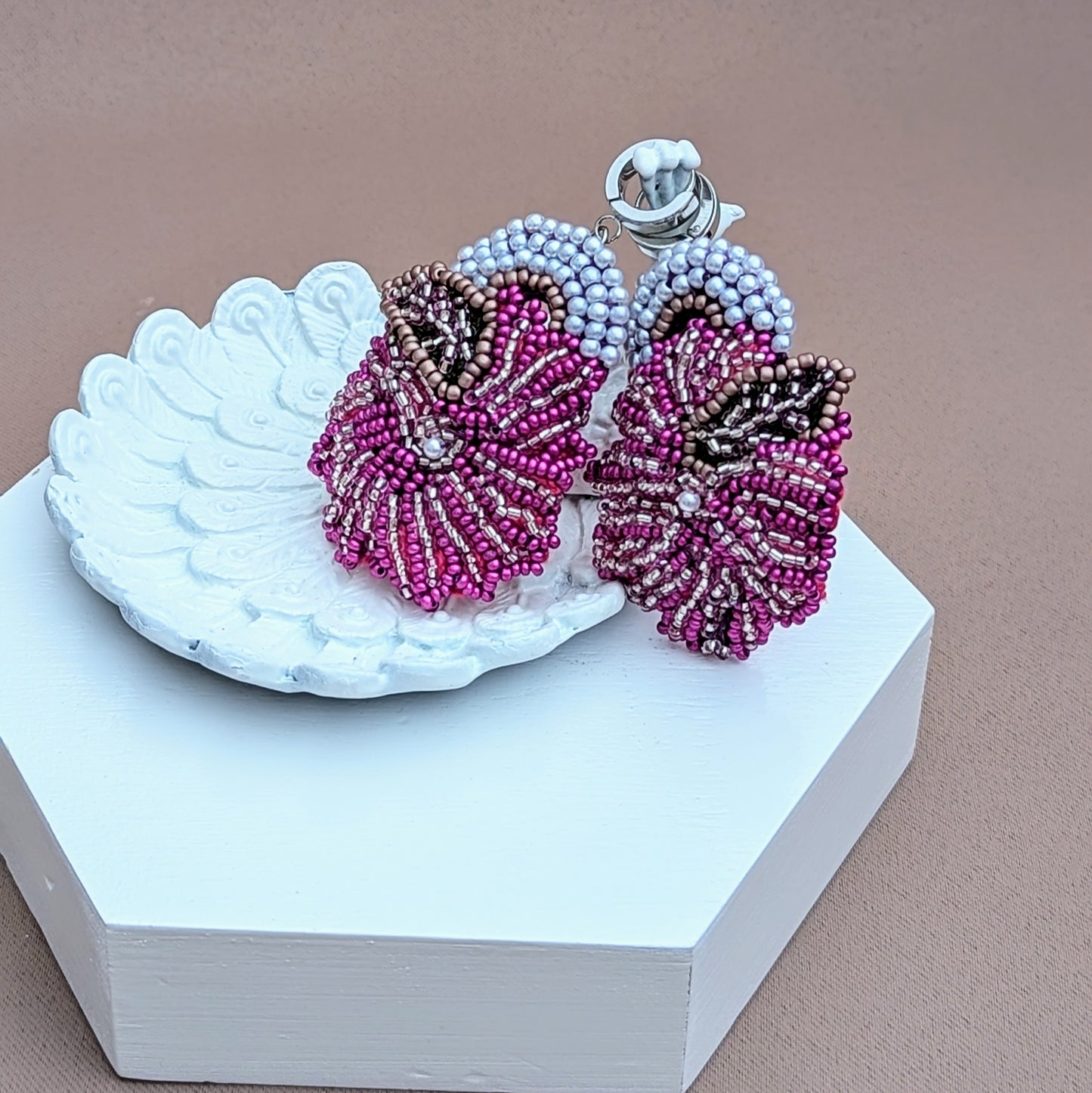 An intricate, heavily bead embroidered unique pair of purple, white and silver Indian earrings exclusively available from sustainable UK brand Mayaani Jewellery. Experience a sumptuous blend of contemporary style and traditional artistry paired with comfort creating the perfect eye-catching statement worthy accessory for extended wear at weddings and special occasions. The vivid magenta floral motif is met perfectly with silver and ivory pearl accents.