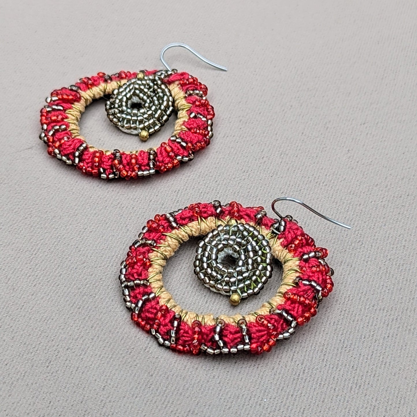 Experience the beauty of traditional artistry with a modern edge with this sustainable pair of red hot sun earrings exclusive to Mayaani Jewellery UK. Featuring high quality upcycled materials intricately hand woven into a circular design with a contrasting metallic silver centre, and gold accents, the strikingly bold and elegant design brings a new dimension to Indian wedding & occasion wear.