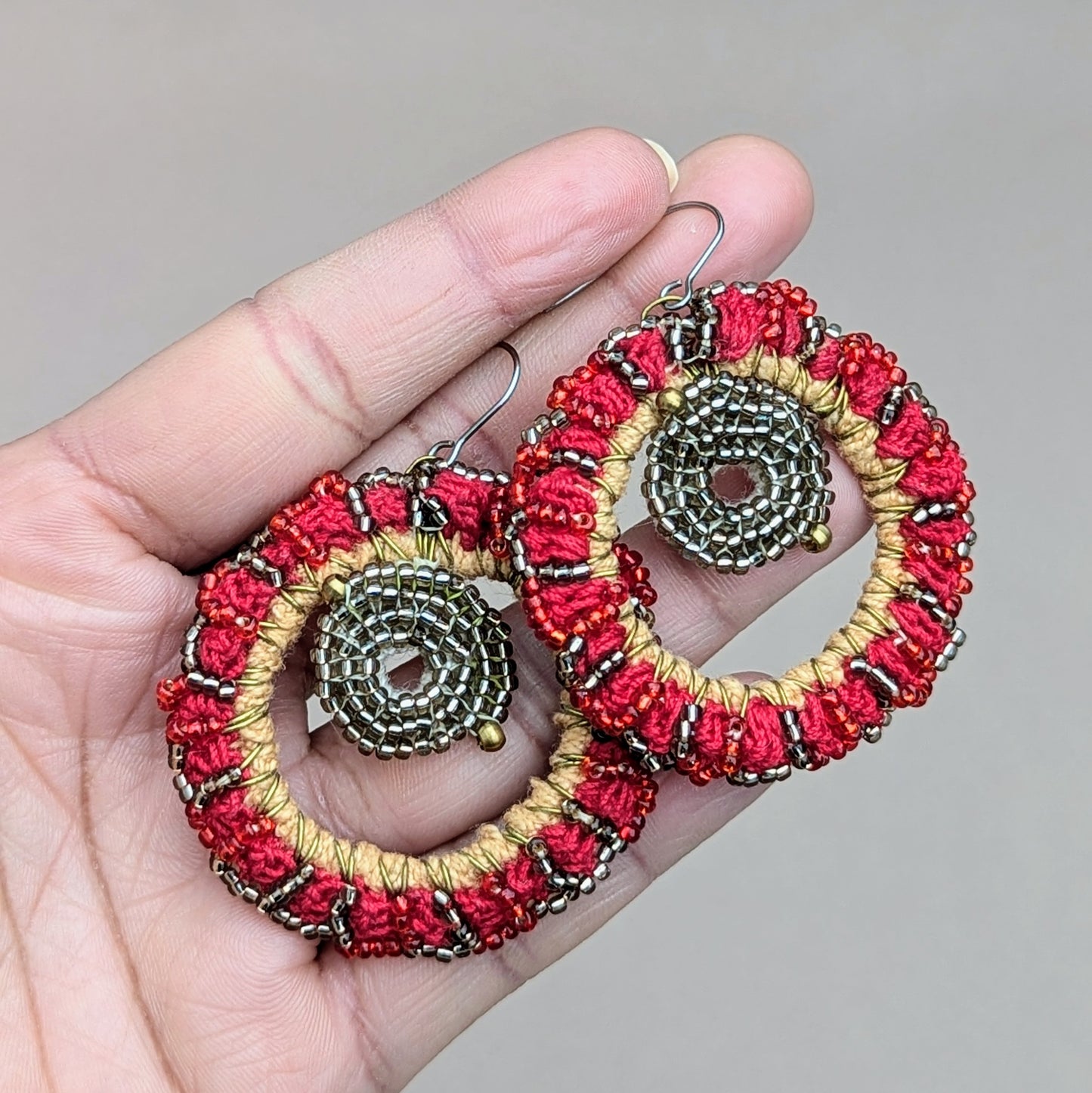 Hand holding a bold vibrant pair of red, silver and gold Indian style circular statement earrings exclusive to sustainable UK brand Mayaani Jewellery. The inclusion of high quality upcycled materials in this show stopping pair demonstrates the brands commitment to sustainability whilst the expert craftsmanship and design celebrate modern fashion and traditional artistry.