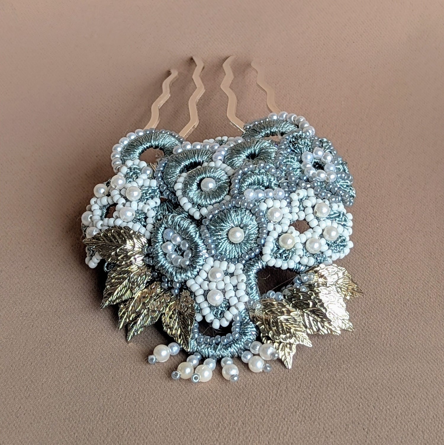 Enhance your bridal and occasion style with this luxurious, one-of-a-kind silver and grey Indian-inspired statement hairpin from the sustainable brand Mayaani Jewellery UK. Featuring a stunning blend of delicate hand crochet, meticulous beadwork, and expert wire wrapping, it showcases metallic silver-grey circles and floral motifs alongside detailed silver-plated leaves for a captivating layered design. Perfect for weddings and special events, this vintage-inspired hairpin embodies femininity.