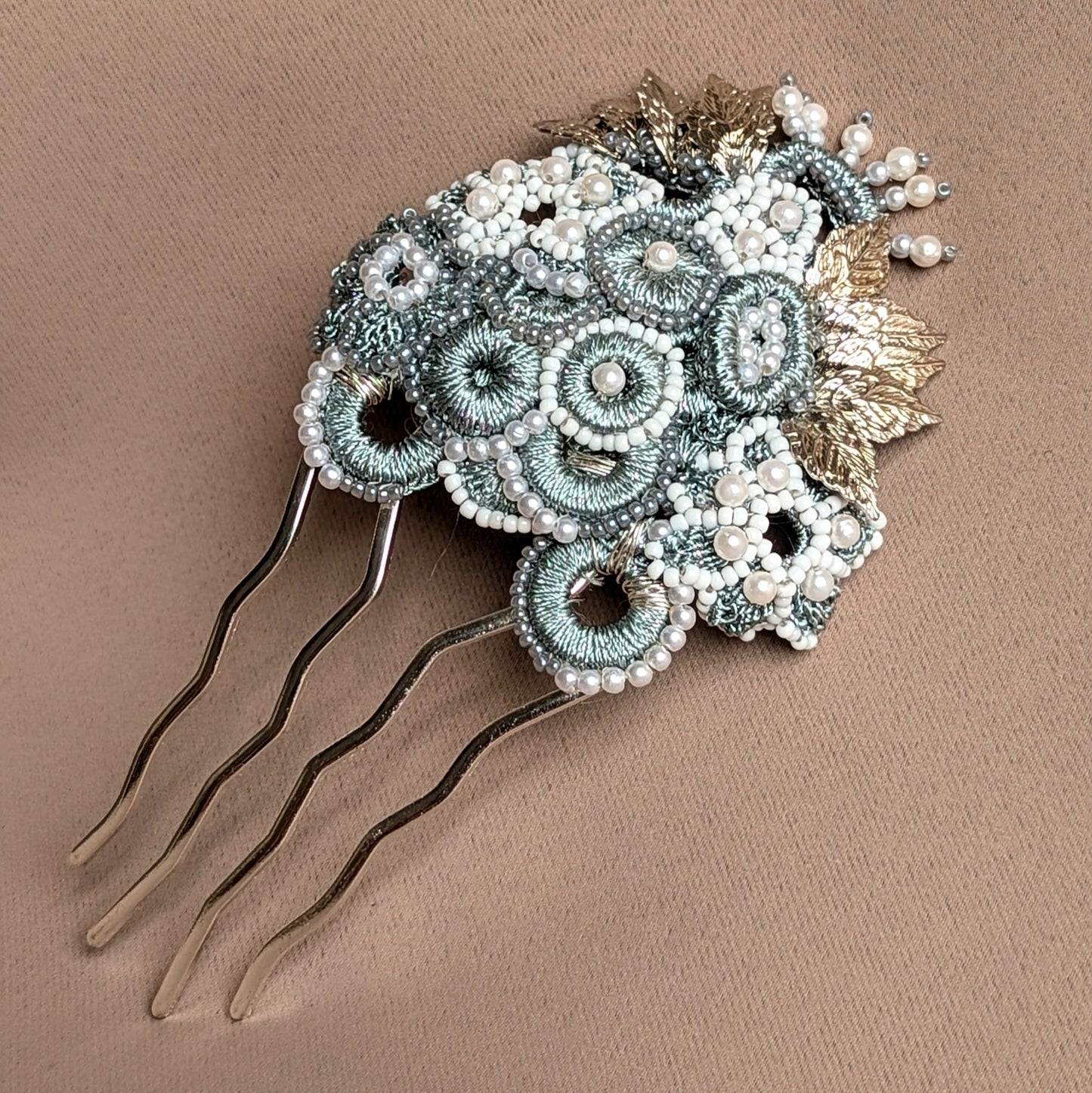 Transform your bridal style with this luxurious, one-of-a-kind silver and grey hairpin from Mayaani Jewellery UK, a sustainable brand. This statement piece features a beautiful combination of hand crochet, detailed beadwork, and expert wire wrapping, showcasing metallic silver-grey circles and floral motifs along with ornate silver-plated leaves. Perfect for weddings and special occasions, this vintage-inspired hairpin radiates feminine sophistication. Complementary matching earrings are also included.