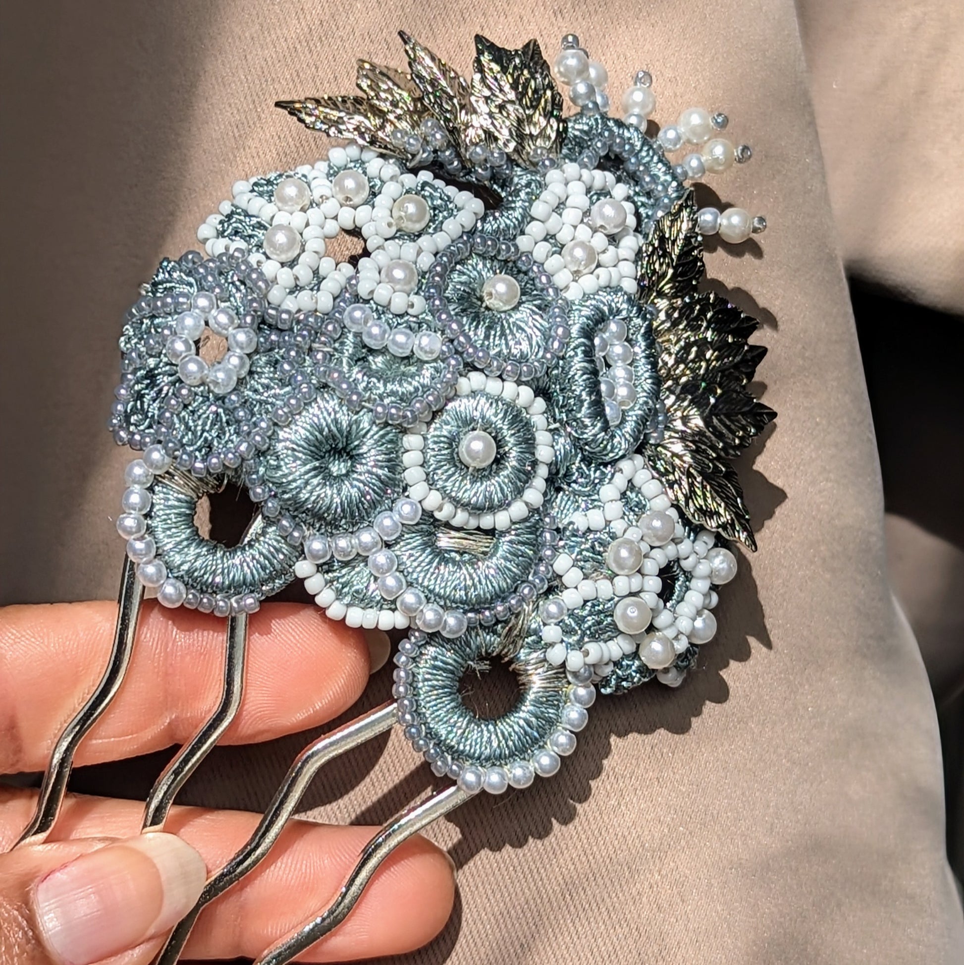 Elevate your wedding and occasion look with this unique silver and grey Indian-inspired statement hairpin by sustainable brand Mayaani Jewellery UK. Featuring a bold blend of delicate hand crochet, intricate beadwork, and expert wire wrapping, the design showcases metallic silver-grey circles and floral motifs accented with detailed silver-plated leaves. This regal, vintage-inspired hairpin embodies feminine elegance and sophistication, perfect for weddings and special events. Matching earrings included.