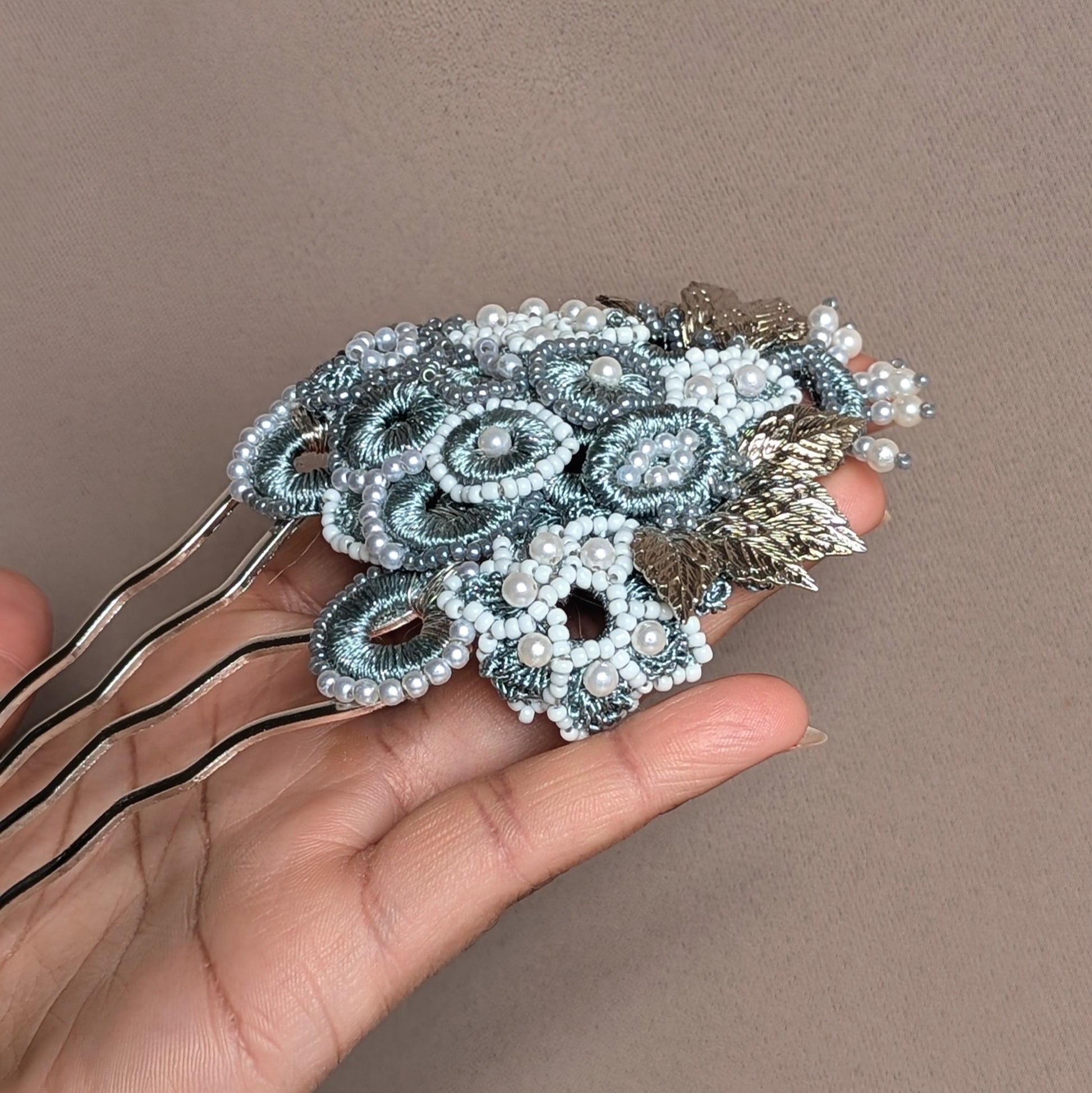 Elevate your style with this luxurious silver and grey statement hairpin from sustainable brand Mayaani Jewellery UK. This one-of-a-kind piece features a beautiful blend of delicate hand crochet, meticulous beadwork, and expert wire wrapping, showcasing metallic silver-grey circles and floral designs accented by silver-plated leaves. Perfect for everything from your wedding day to special events, this vintage-inspired hairpin exudes feminine sophistication, complete with matching earrings.