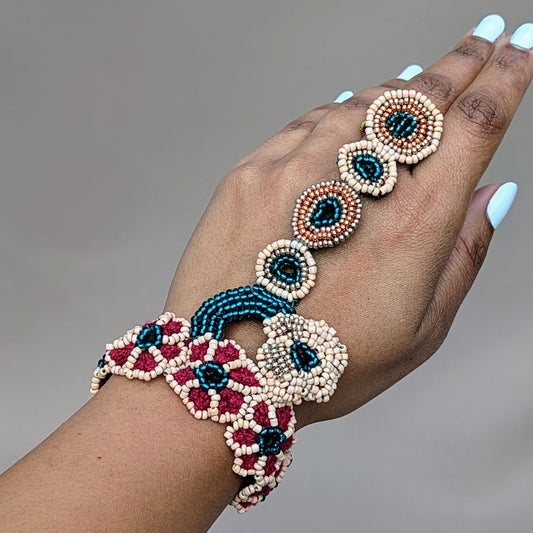 Hand modelling a unique designer made Indian bridal hand bracelet / haath phool exclusive to Mayaani Jewellery, a sustainable UK brand. Featuring intricate hand beadwork in emerald green, peach, gold and rose gold tones, arranged in a circular and floral design. It connects the wrist to the finger with a delicate chain of beaded rings, showcasing detailed hand crochet and wire wrapping. A versatile piece that pairs with the matching bridal set or can be worn independently for weddings or formal events.