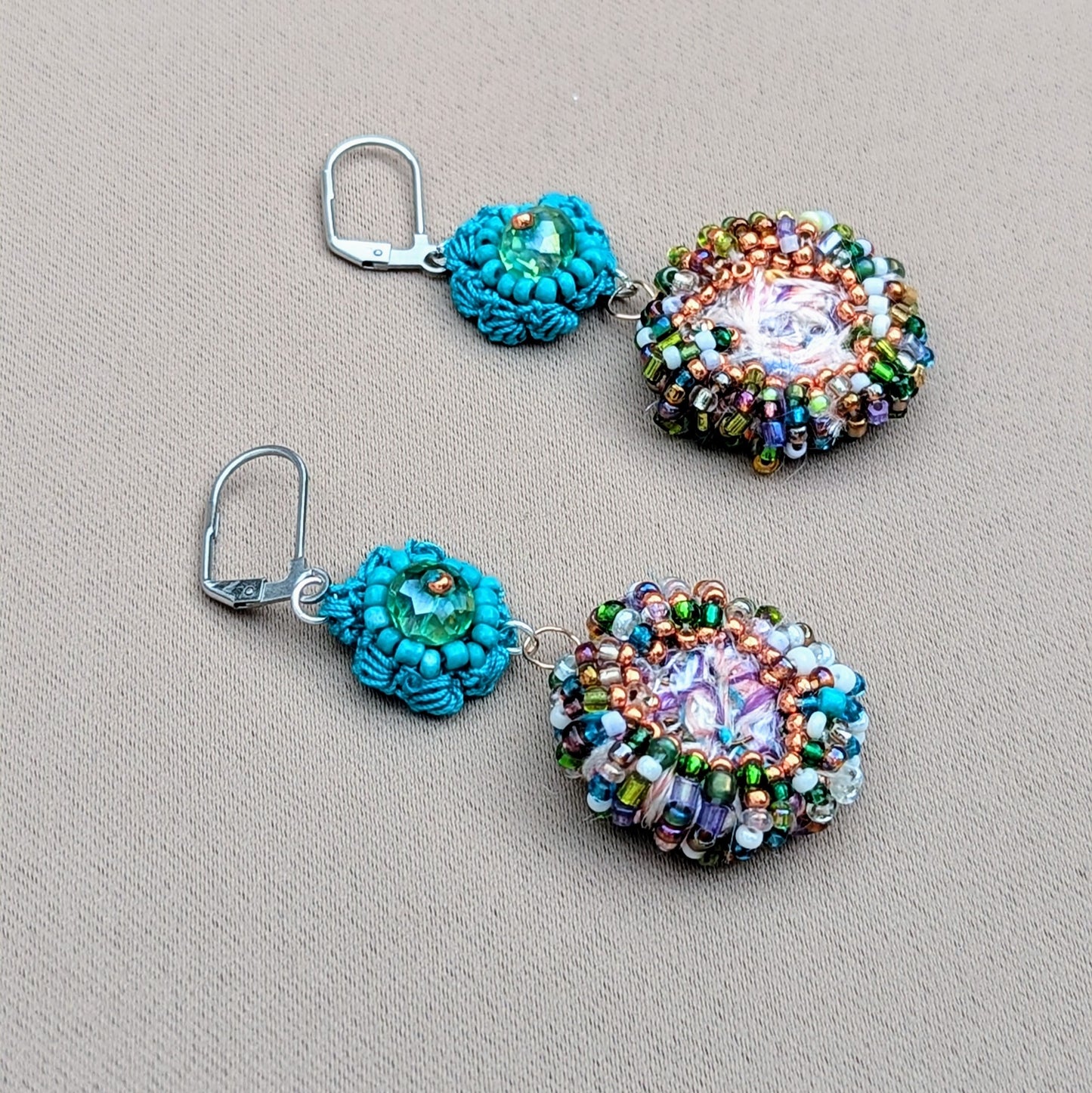 A pair of eco-friendly scrap bead earrings from Mayaani Jewellery UK, inspired by ocean hues and Indian design. Each features a large circular scrap bead (handmade from jewellery making remnants), colourful upcycled seed beads, and a turquoise flower motif, perfect for special occasions or everyday wear.