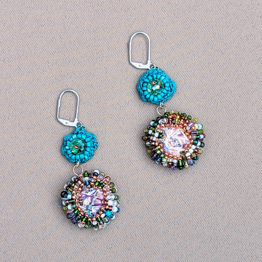 A pair of sustainable scrap bead earrings from Mayaani Jewellery UK, inspired by crystal-clear ocean waters and Indian design. Each earring features a large circular scrap bead handcrafted from remnants of the jewellery-making process, accented with high-quality upcycled seed beads in purple, rose gold, green, white, and blue. A hand-crocheted turquoise flower motif with an upcycled Swarovski-style bicone bead completes the look. Wedding and occasion perfect they pair comfortably with everyday.