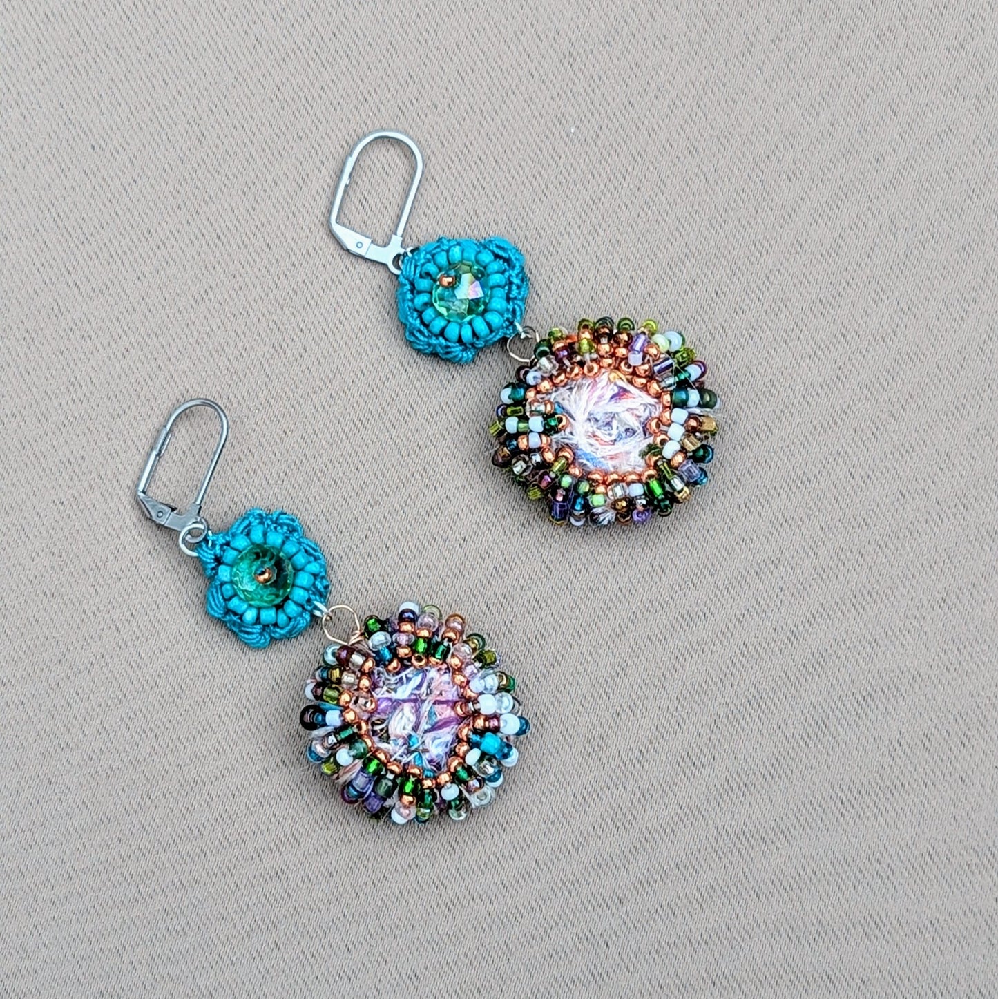 Beautiful sustainable scrap bead earrings by Mayaani Jewellery UK, drawing inspiration from crystal-clear ocean waters and Indian design. Each earring showcases a large circular scrap bead, carefully handcrafted from remnants of the jewellery-making process, and features an array of vibrant upcycled seed beads. A charming hand-crocheted turquoise flower motif, accented with an upcycled Swarovski-style bicone bead, adds the finishing touch. Ideal for weddings and occasions, they also enhance everyday outfits