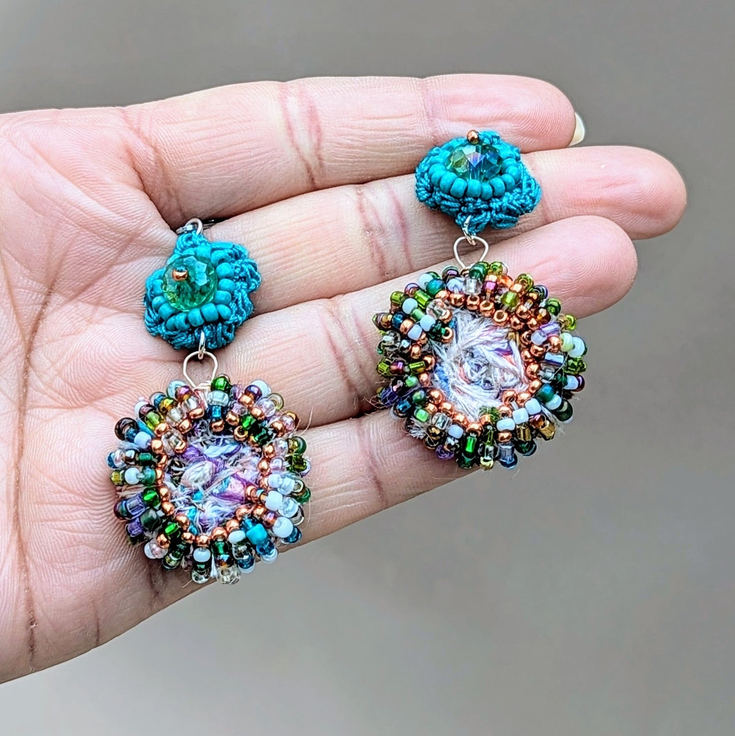 A striking pair of sustainable scrap bead earrings from Mayaani Jewellery UK, inspired by the tranquil colours of crystal-clear ocean waters and Indian artistry. Each earring features a circular scrap bead, handcrafted from leftover materials, beautifully accented with upcycled seed beads in purple, rose gold, green and blue. A hand-crocheted turquoise flower motif with an upcycled Swarovski-style bicone bead completes the ensemble. Perfect for weddings and special occasions, through to everyday wear.