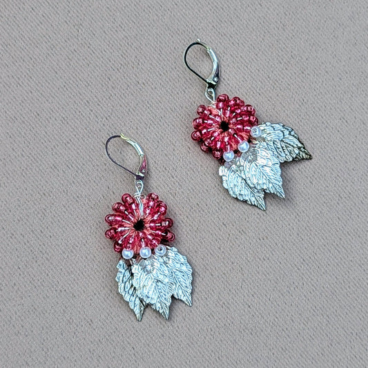 A limited edition pair of watermelon red earrings available in a small range of one off colours exclusive to sustainable UK brand Mayaani Jewellery. This pair features a pink hand crochet base adorned with hand wire wrapped watermelon red and ivory pearl seed beads. Delicately finished with detailed silver plated leaf charms and 925 stamped sterling silver clasps. This Indo-Western inspired pair of earrings add an elegant playful nature inspired touch to every outfit.